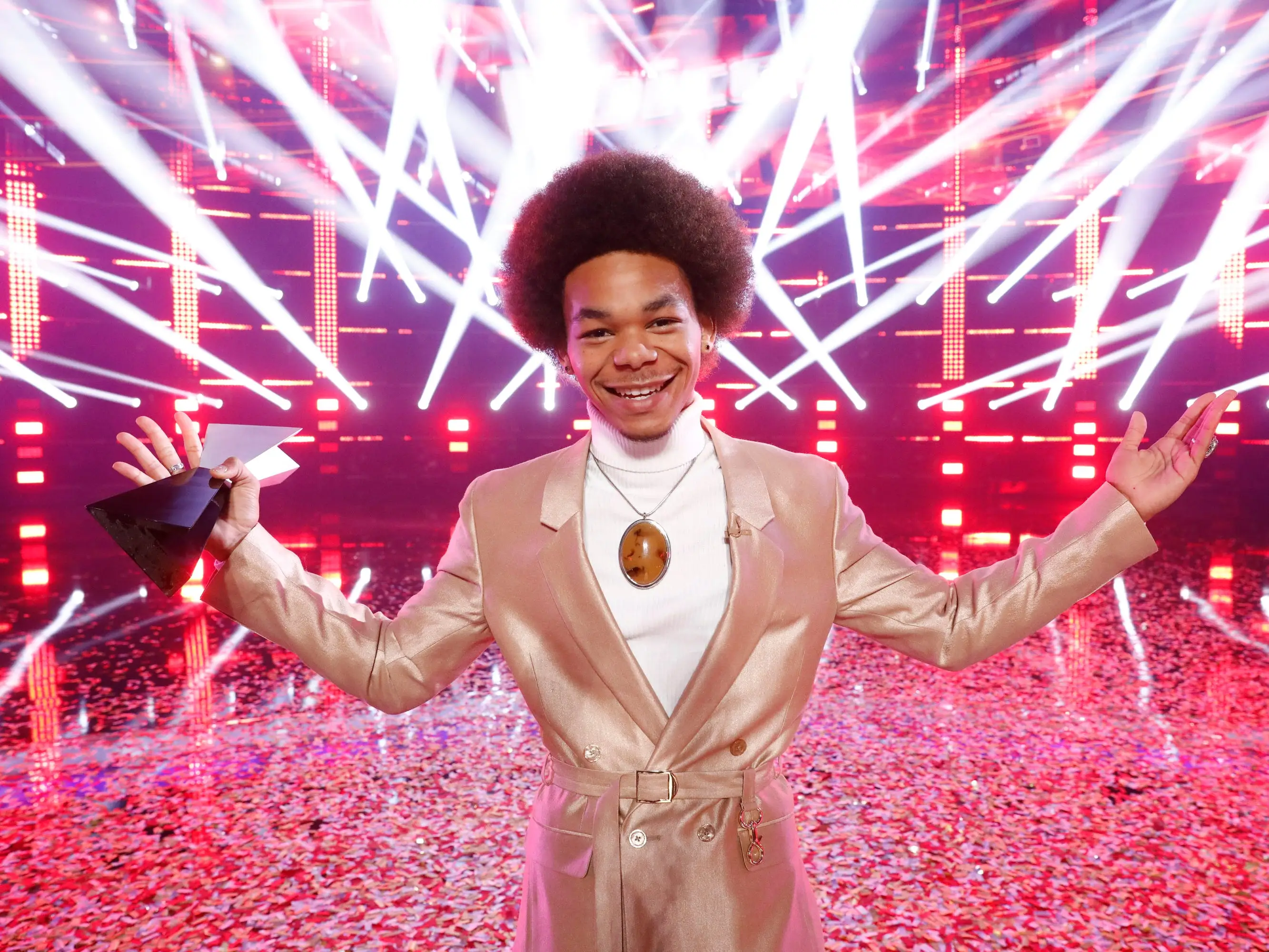 Cam Anthony holding his winning trophy in front of a red, strobe-light background on 