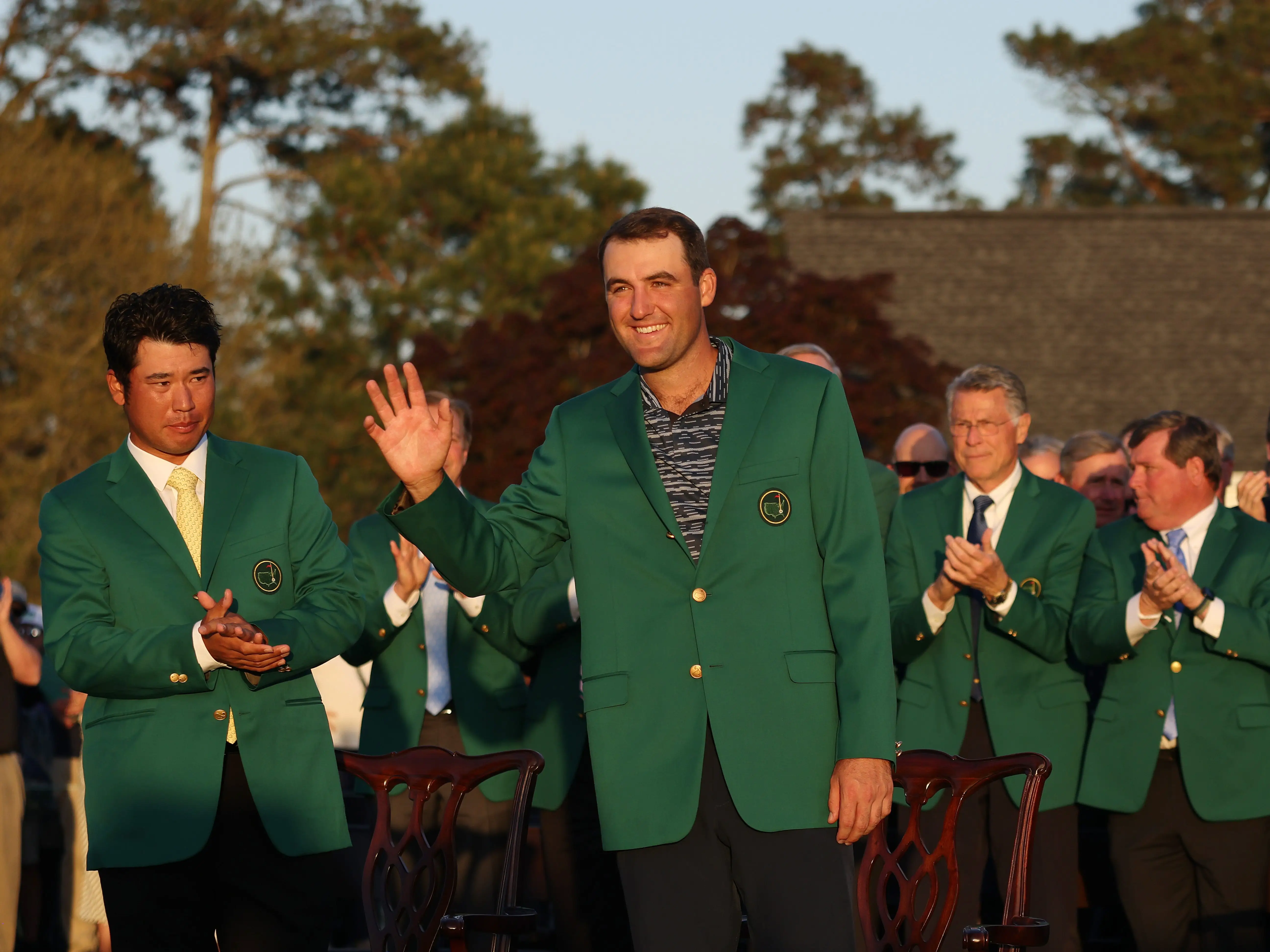 Scottie Scheffler waves to the crowd after being awarded the Green Jacket by 2021 Masters champion Hideki Matsuyama of Japan during the Green Jacket Ceremony after winning the Masters at Augusta National Golf Club on April 10, 2022.