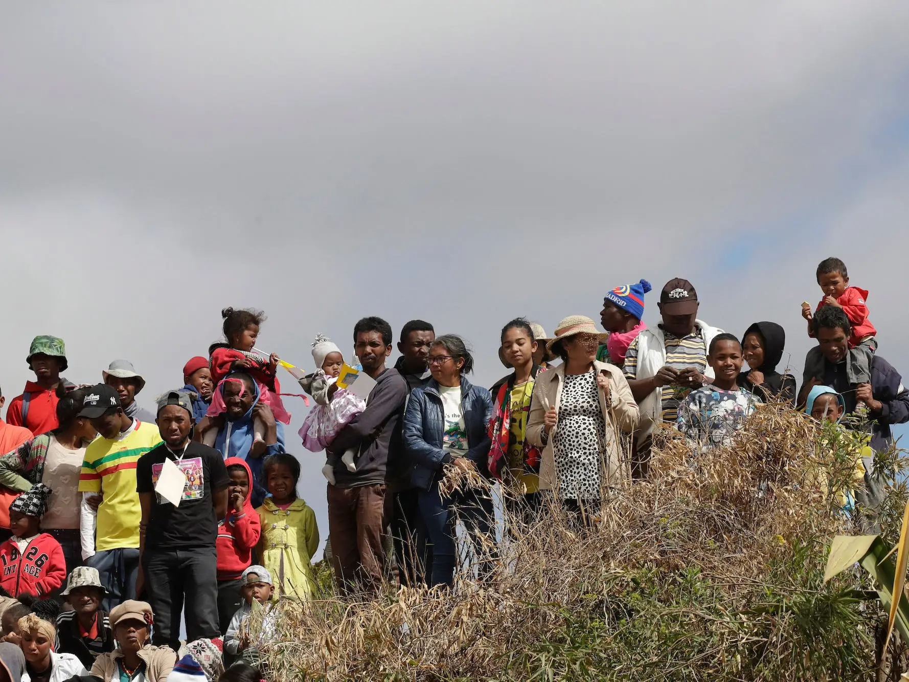 A crowd of people on a grassy hill against a cloudy sky wait for the arrival of Pope Francis on the occasion of his visit to the City of Friendship in Akamasoa, Madagascar, Sunday, Sept. 8, 2019.