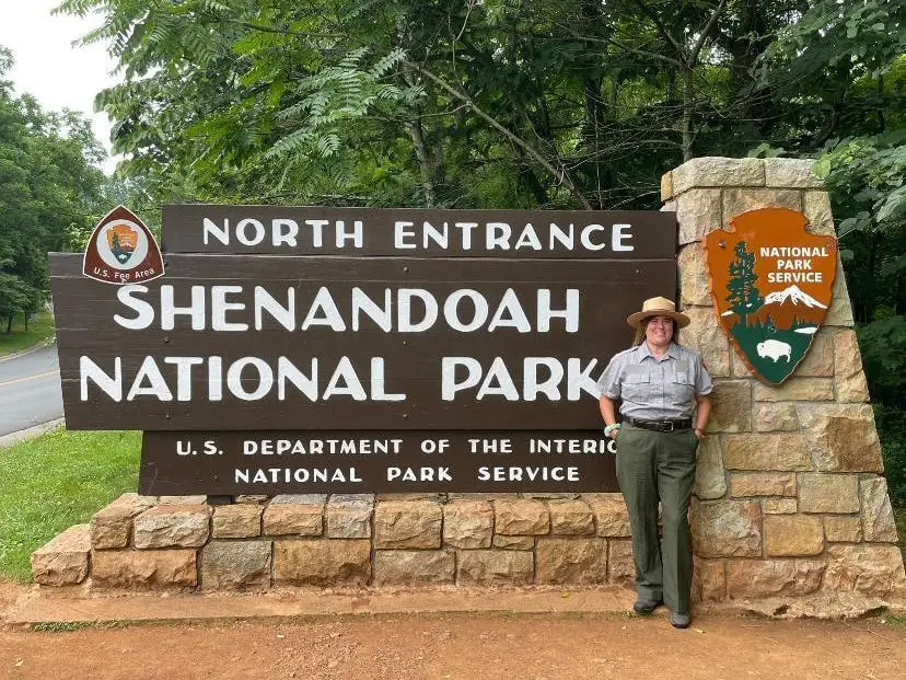 Danielle, in a park ranger uniform, standing at a sign that reads 