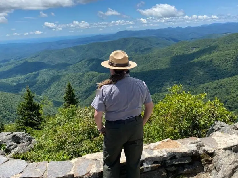 Danielle, wearing a park ranger uniform, looks out at lush mountains covered in greenery.
