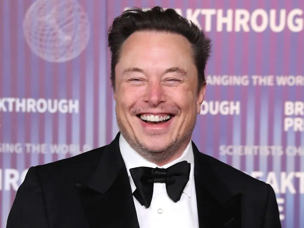 Elon Musk in black tie, laughing.