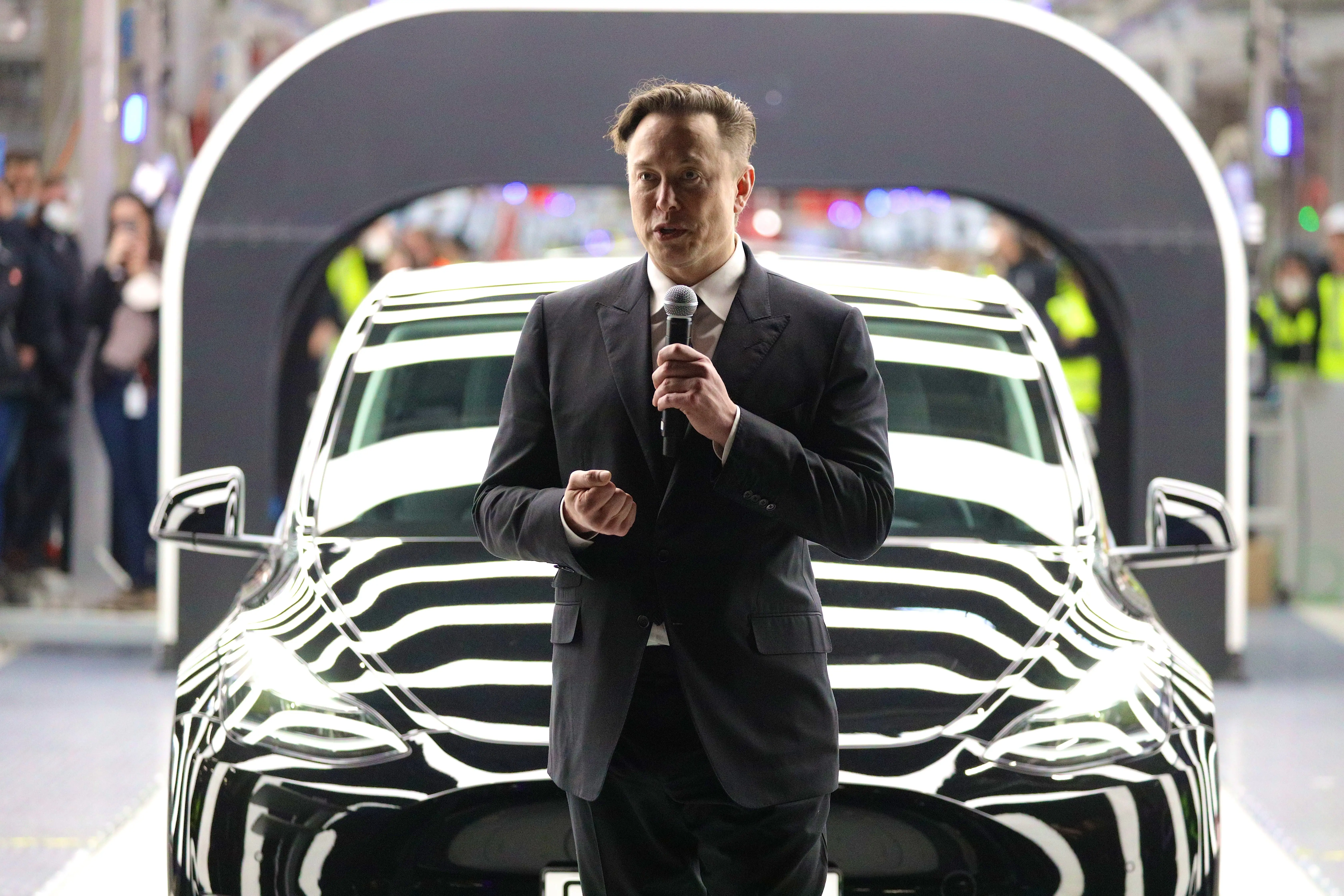 Elon Musk holding a microphone in front of a Tesla.