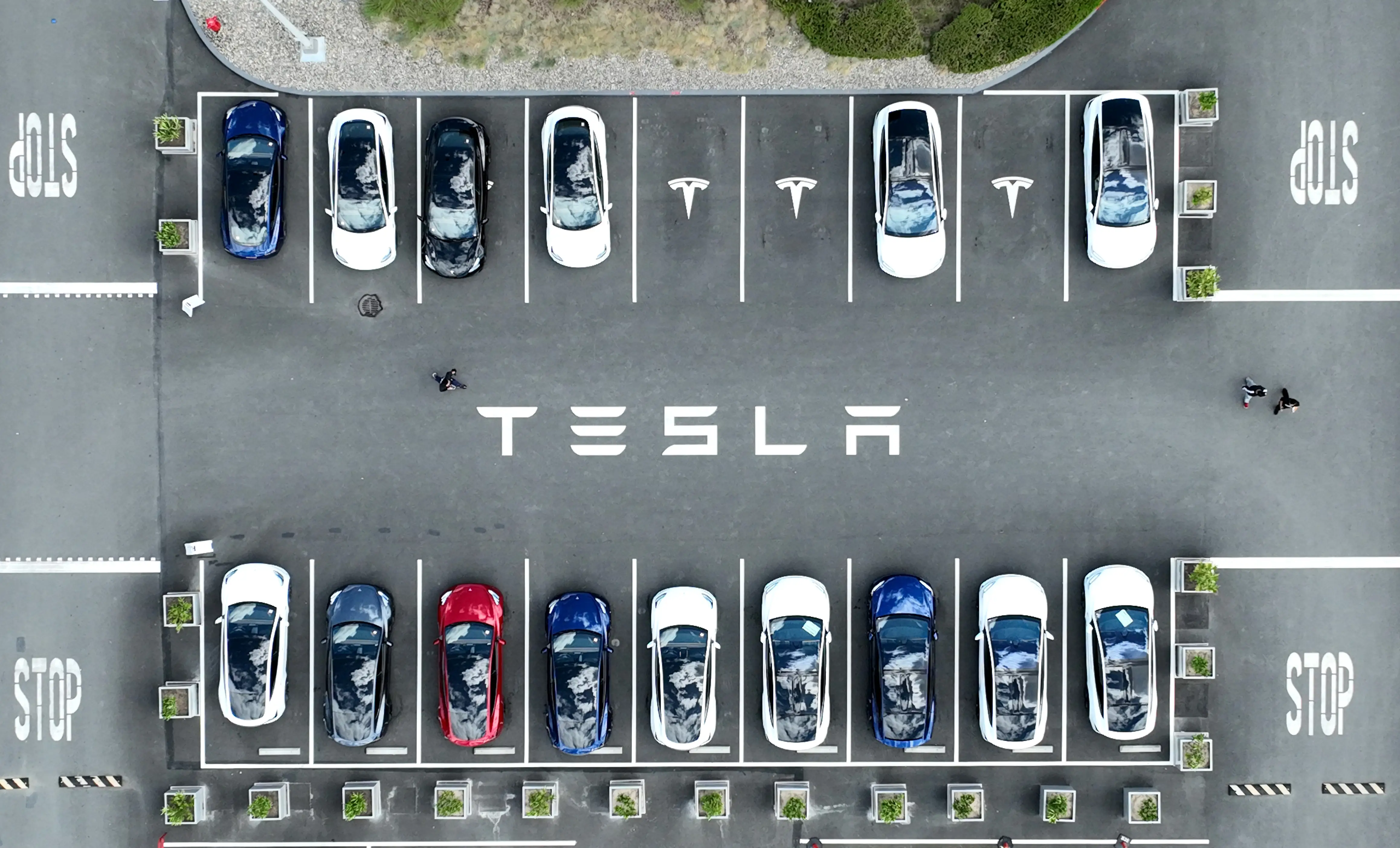 Aerial shot of Tesla vehicles in a car parking lot with Tesla's logo displayed on the road