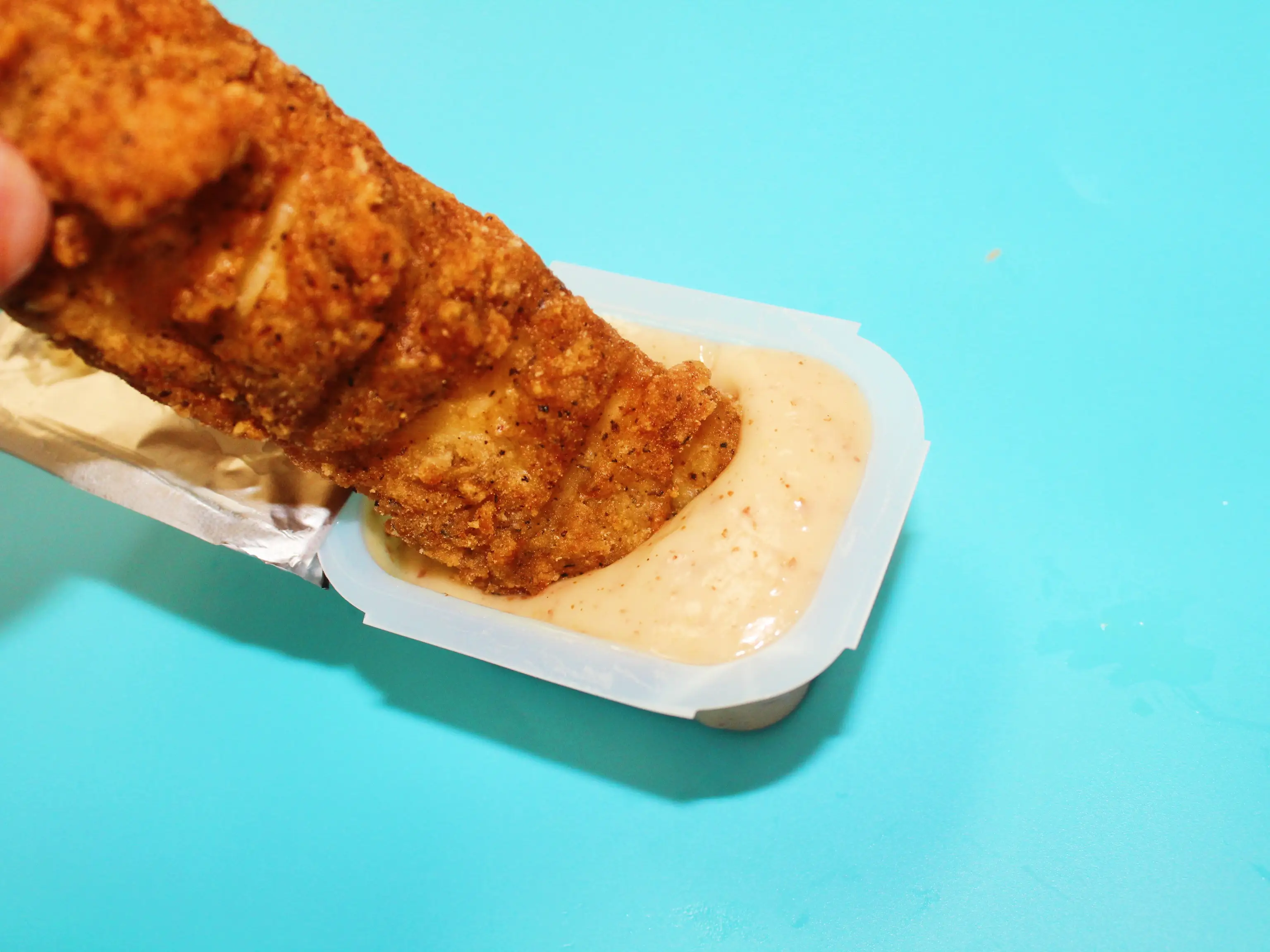 kfc chicken tender dipped in honey mustard on a blue background