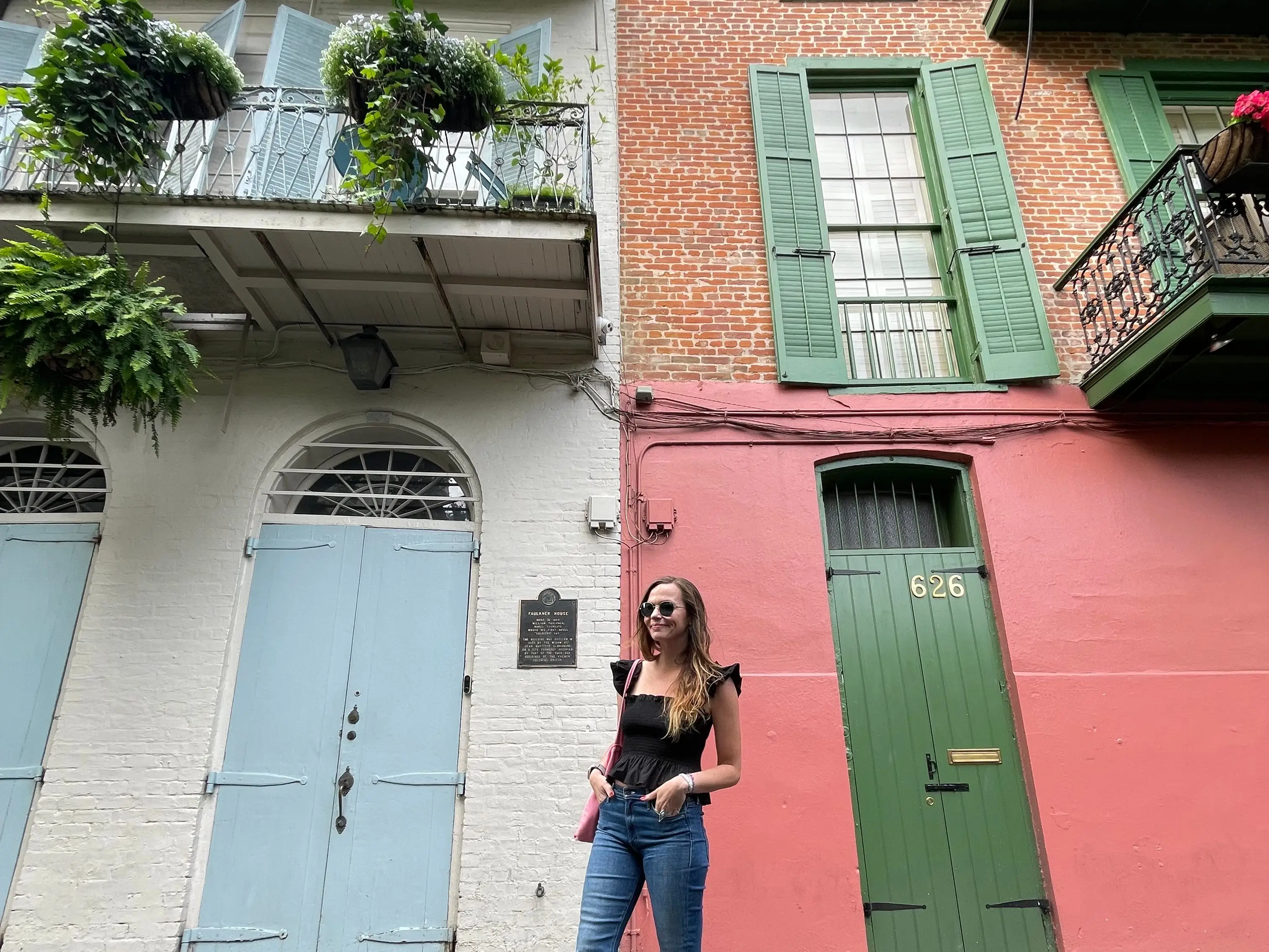Emily poses with her hands in her pockets in front of colorful buildings with balconies in New Orleans.