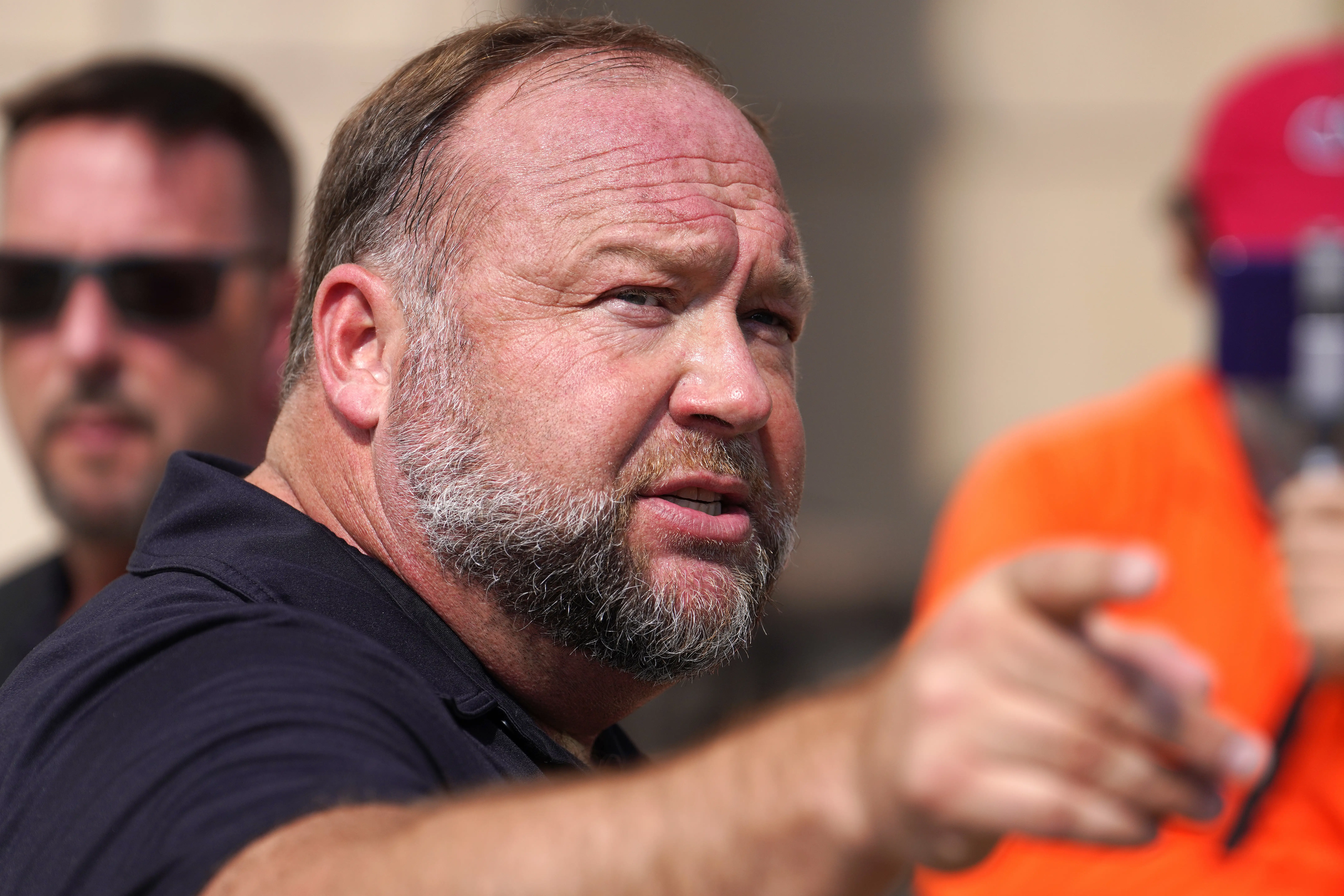 InfoWars founder Alex Jones speaks to the media outside court in Connecticut in 2022, pointing his finger and wearing a blue polo shirt.