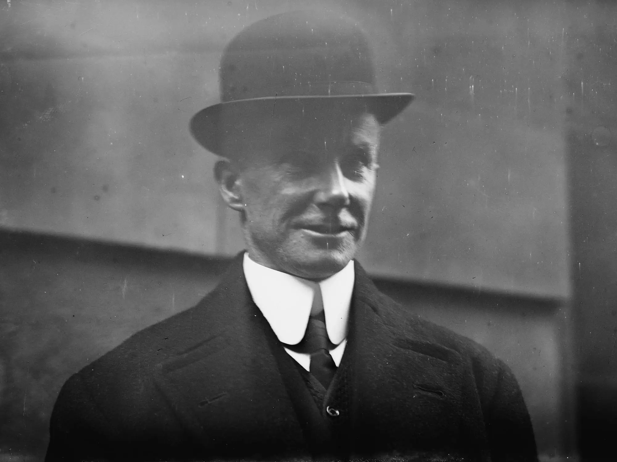 A man in a black bowler hat and suit with a high collar on his white shirt