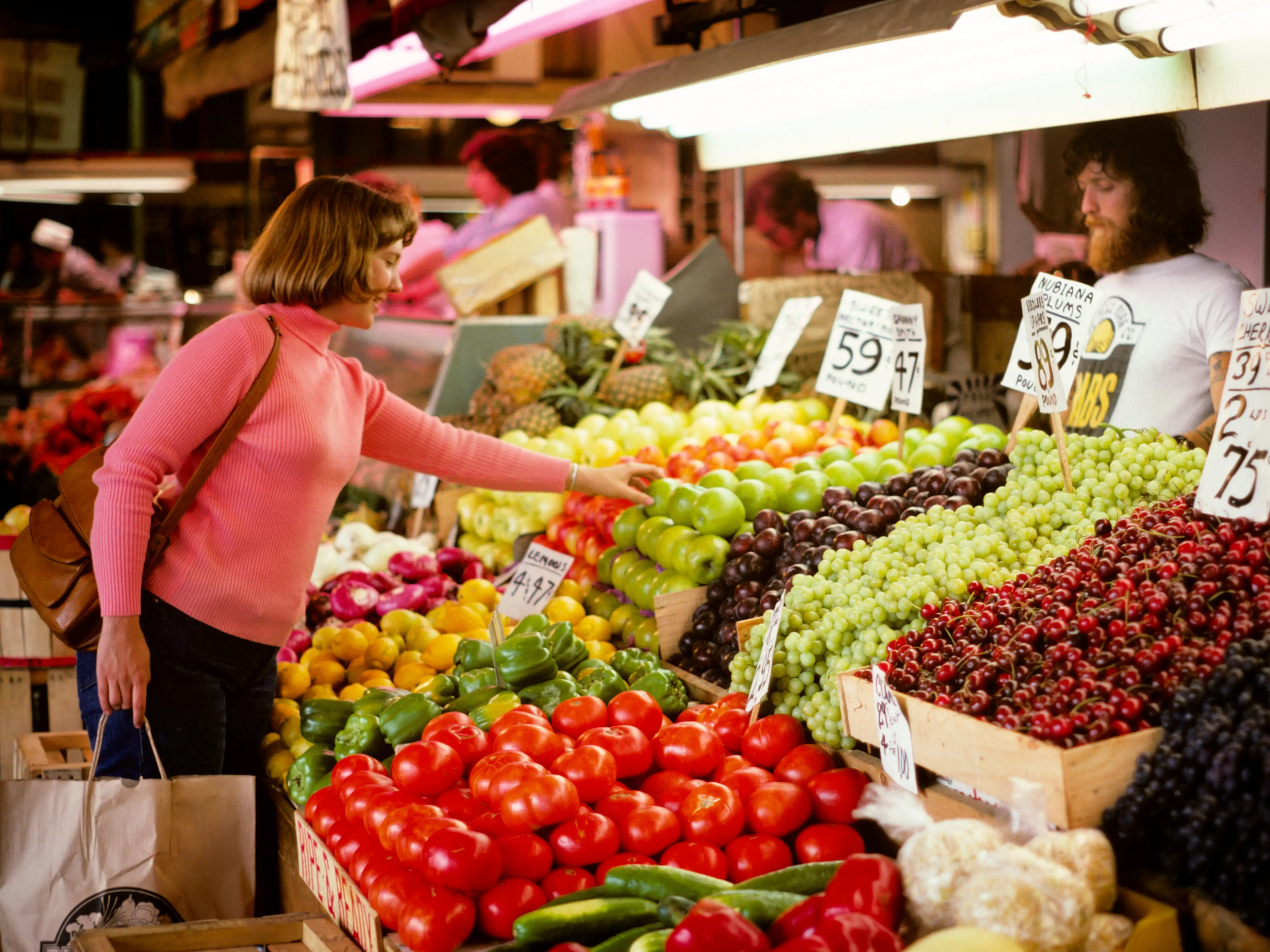 A woman shopping for produce at a market stand in the 1970s.