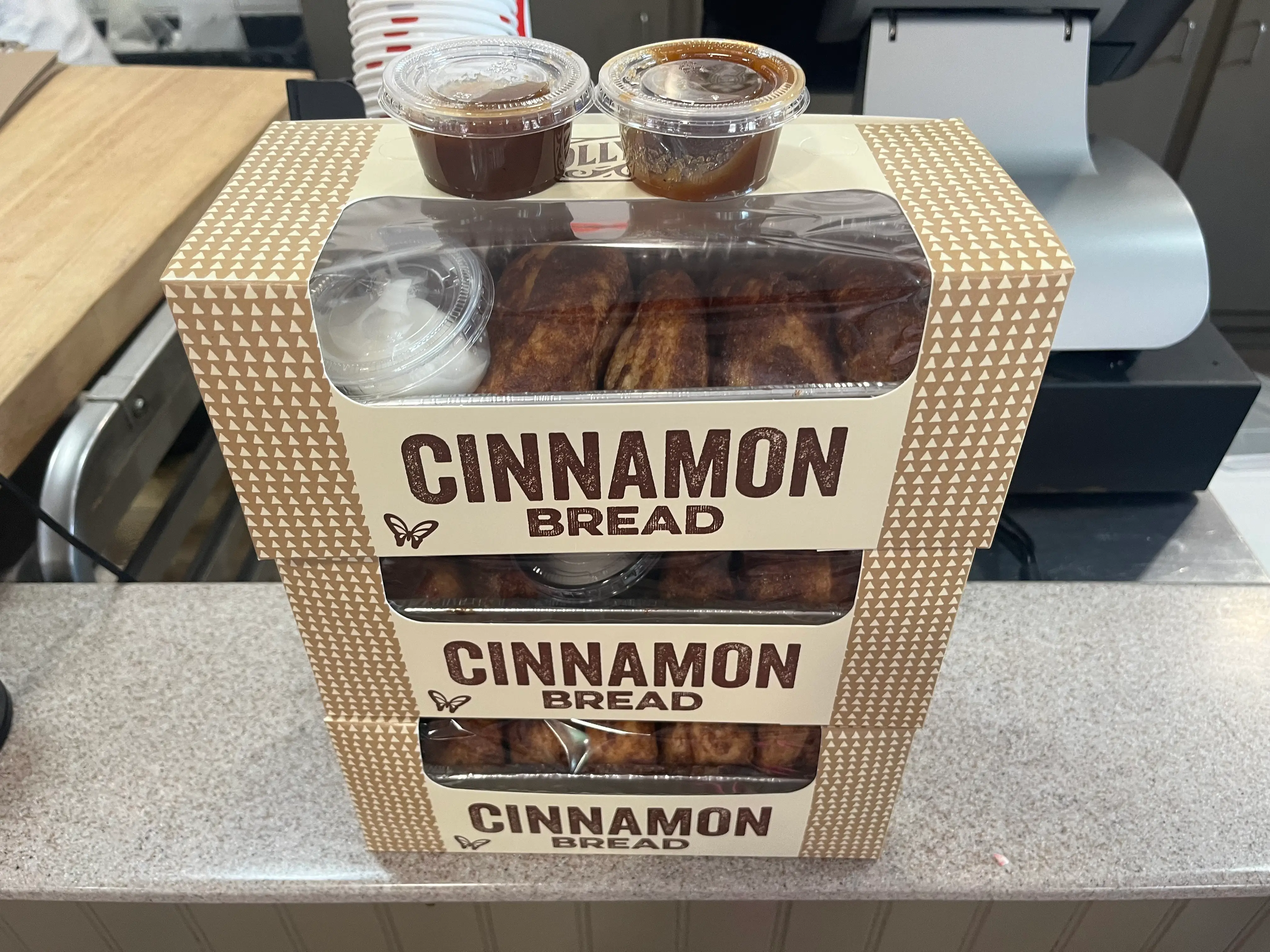 Three stacked boxes of cinnamon bread with sauces in plastic containers on top.