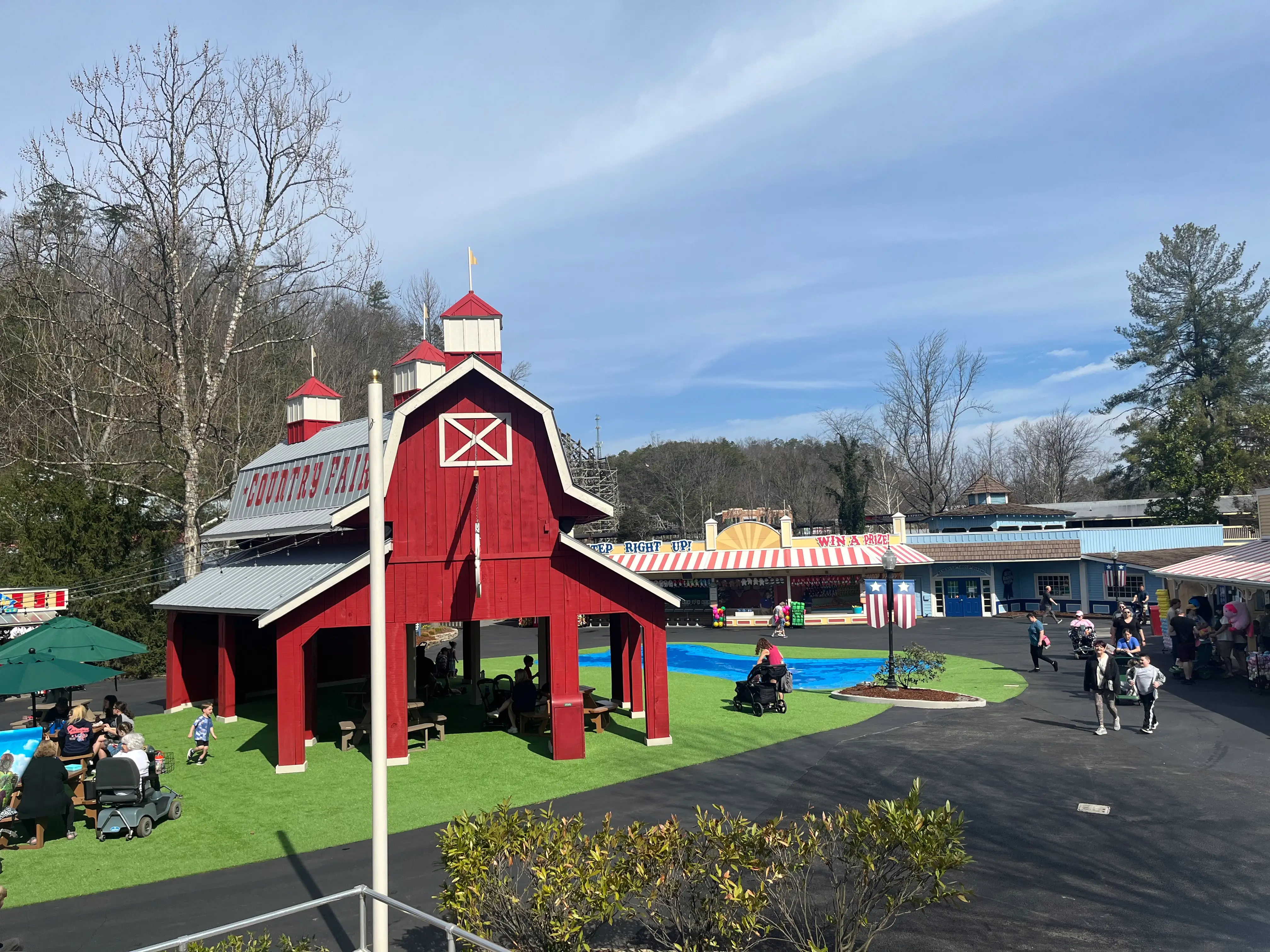 People walking around the Country Fair area of Dollywood, with a red barn-like structure.