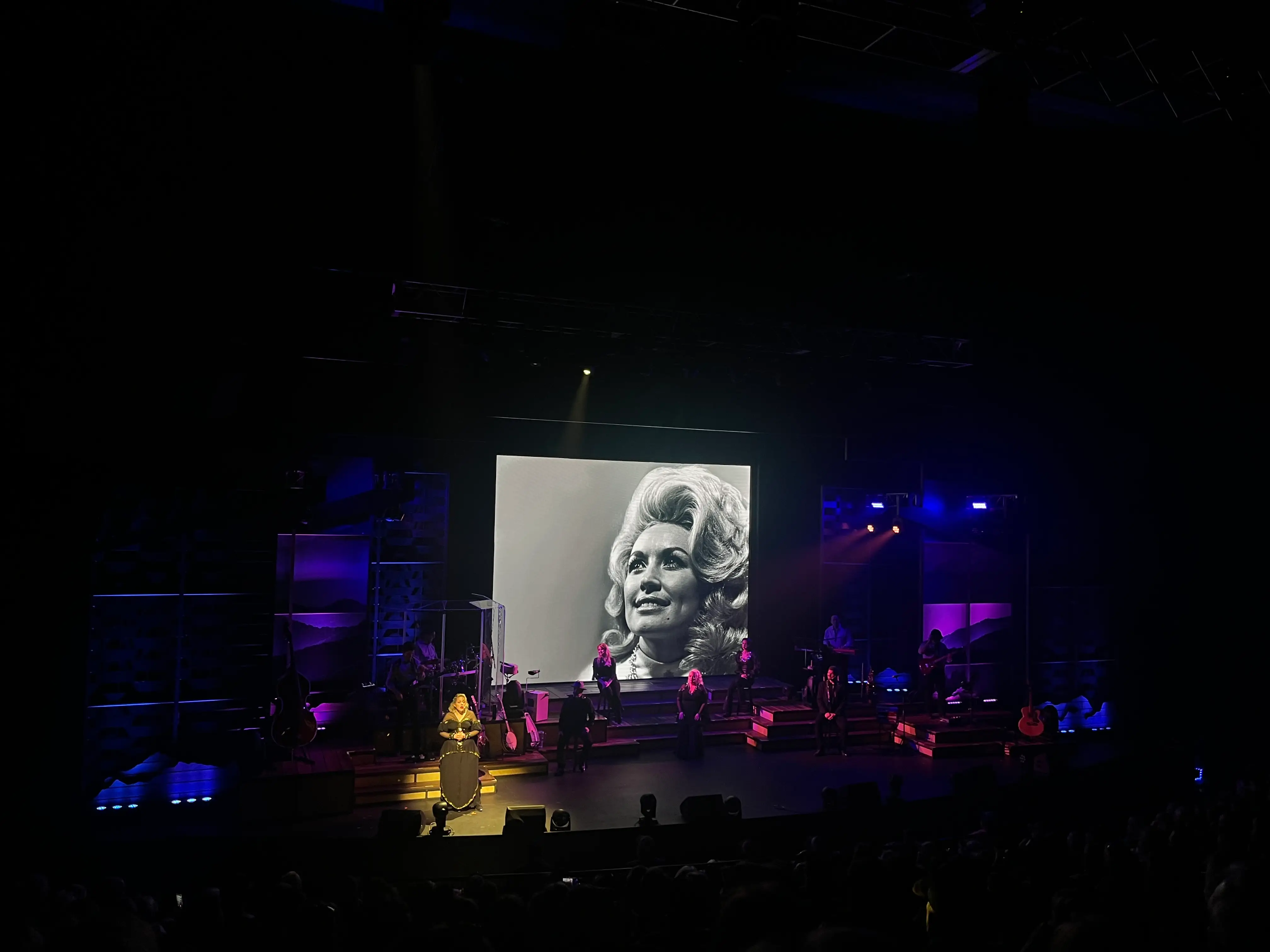 Heidi Parton onstage with a picture of young Dolly Parton on a screen behind her.