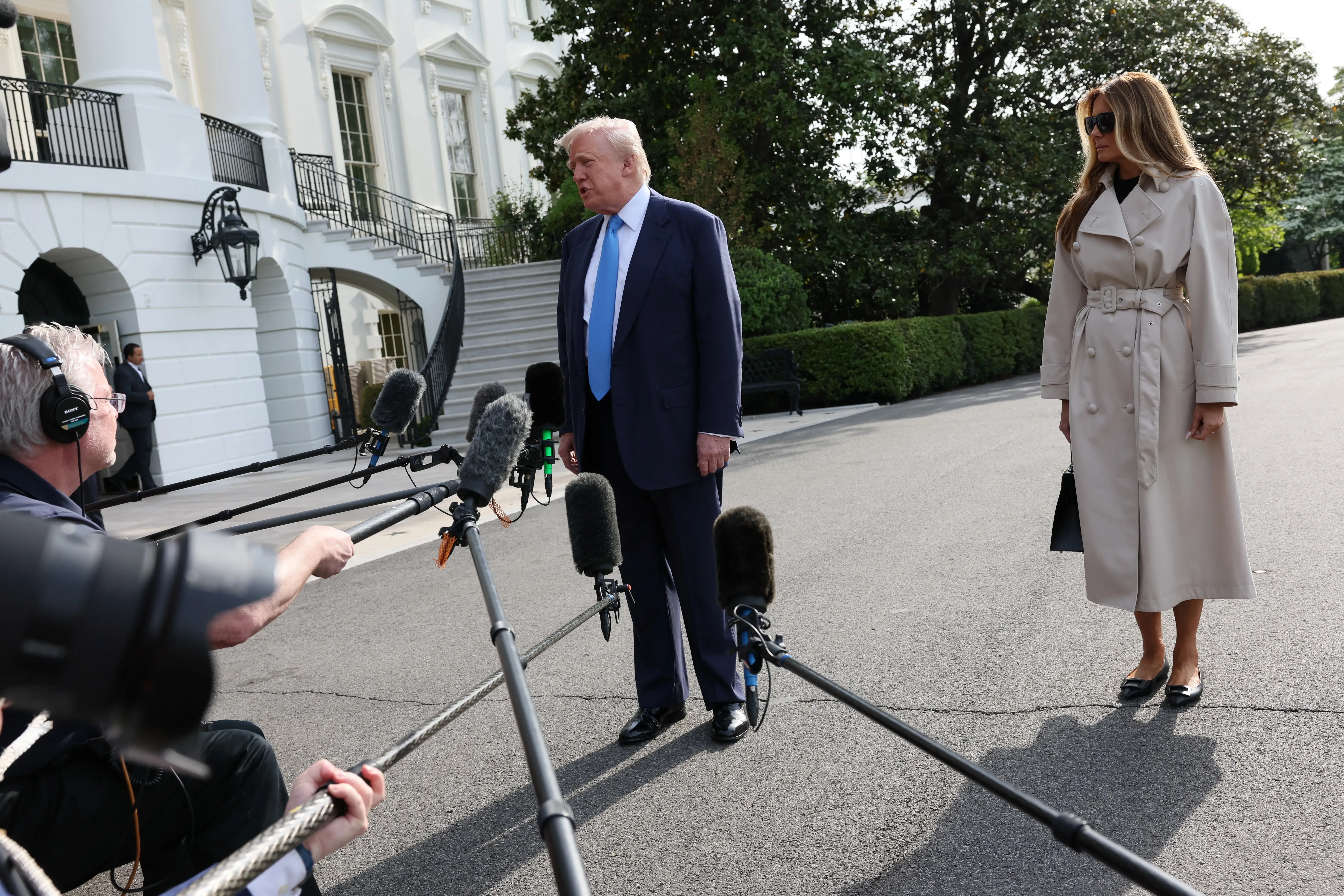 Donald Trump speaks to the press as Melania Trump stands in the background.