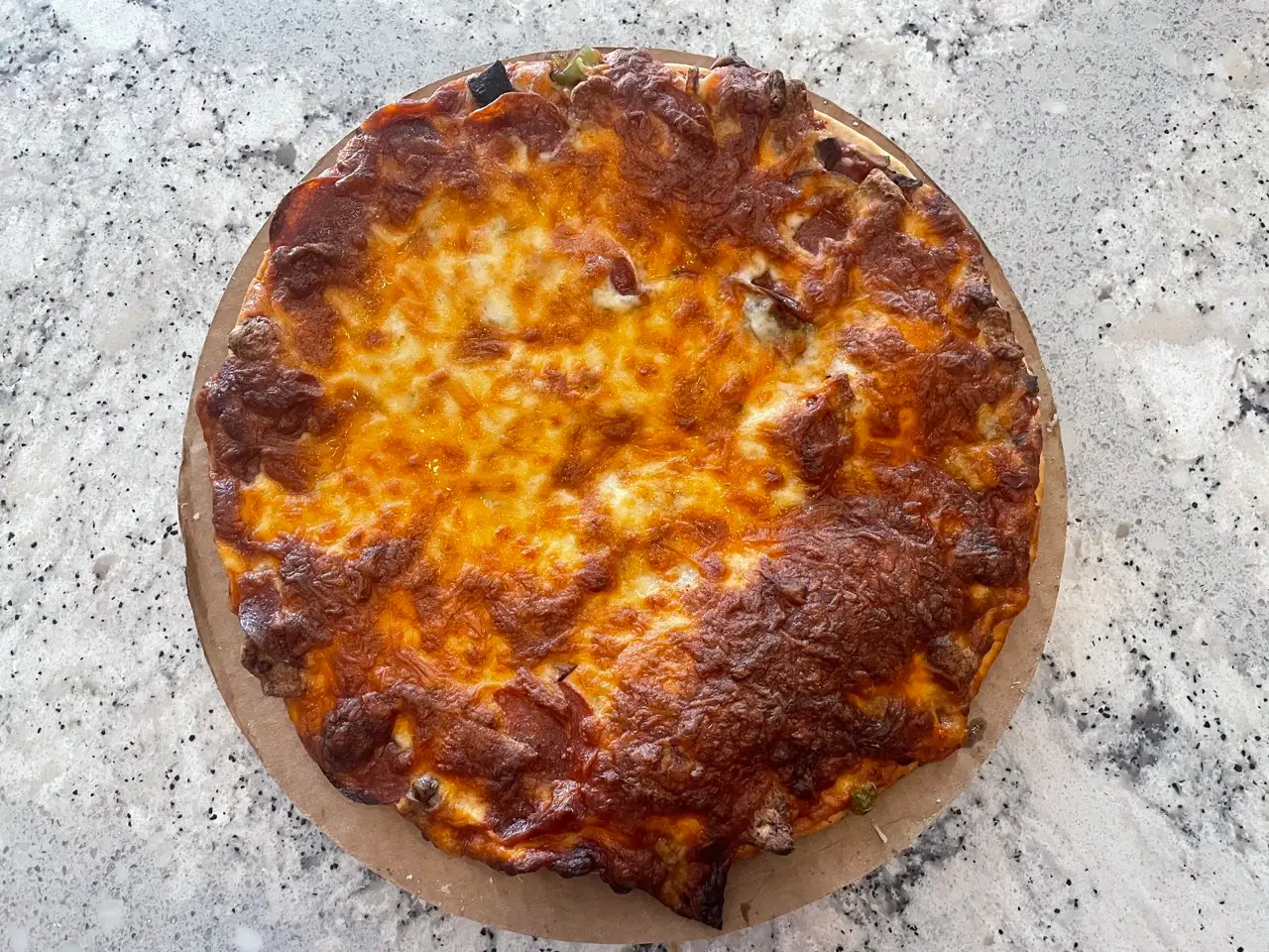 Pizza topped with golden-brown cheese with some vegetables peeking out of sides of the cheese edges