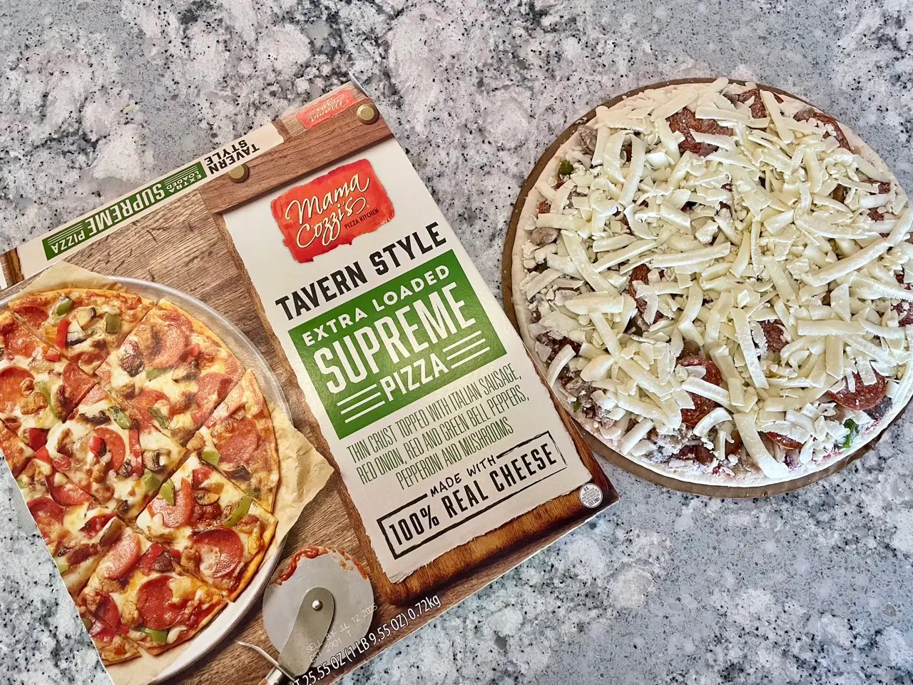 A Mama Cozzi's tavern-style extra-loaded supreme pizza box on counter next to frozen pizza topped with shredded cheese, pepperoni below shreds