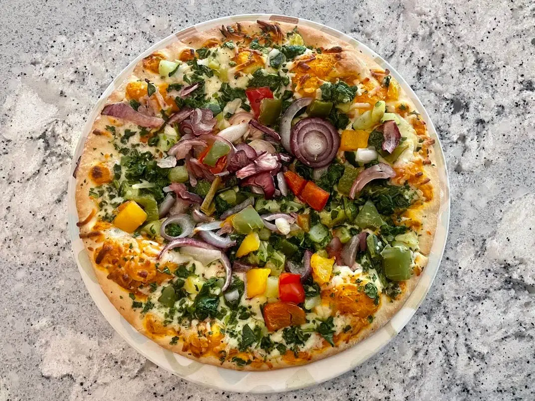 Pizza loaded with vegetables on white counter