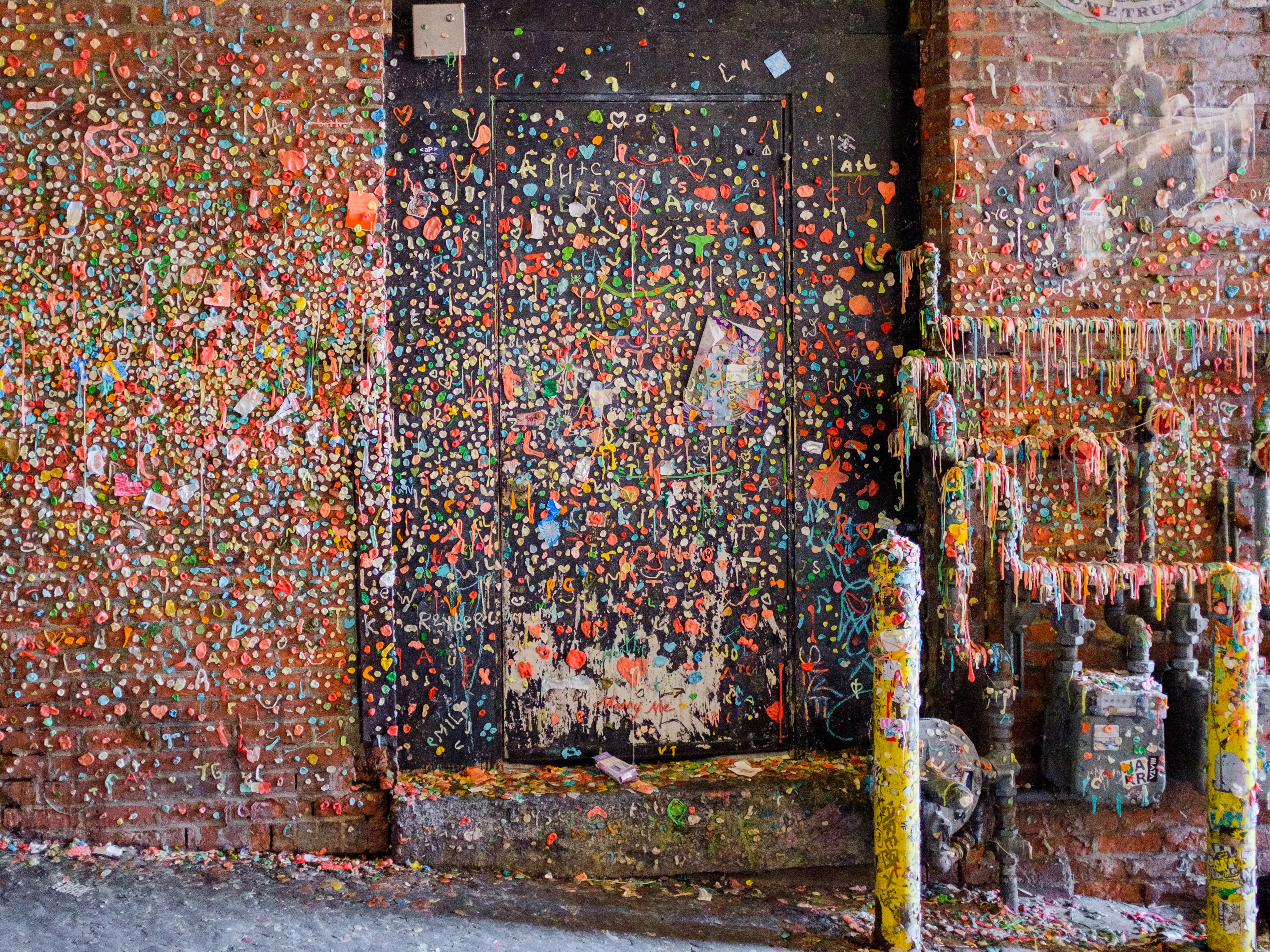 A brick wall in an alleyway is covered in wads of chewed gum