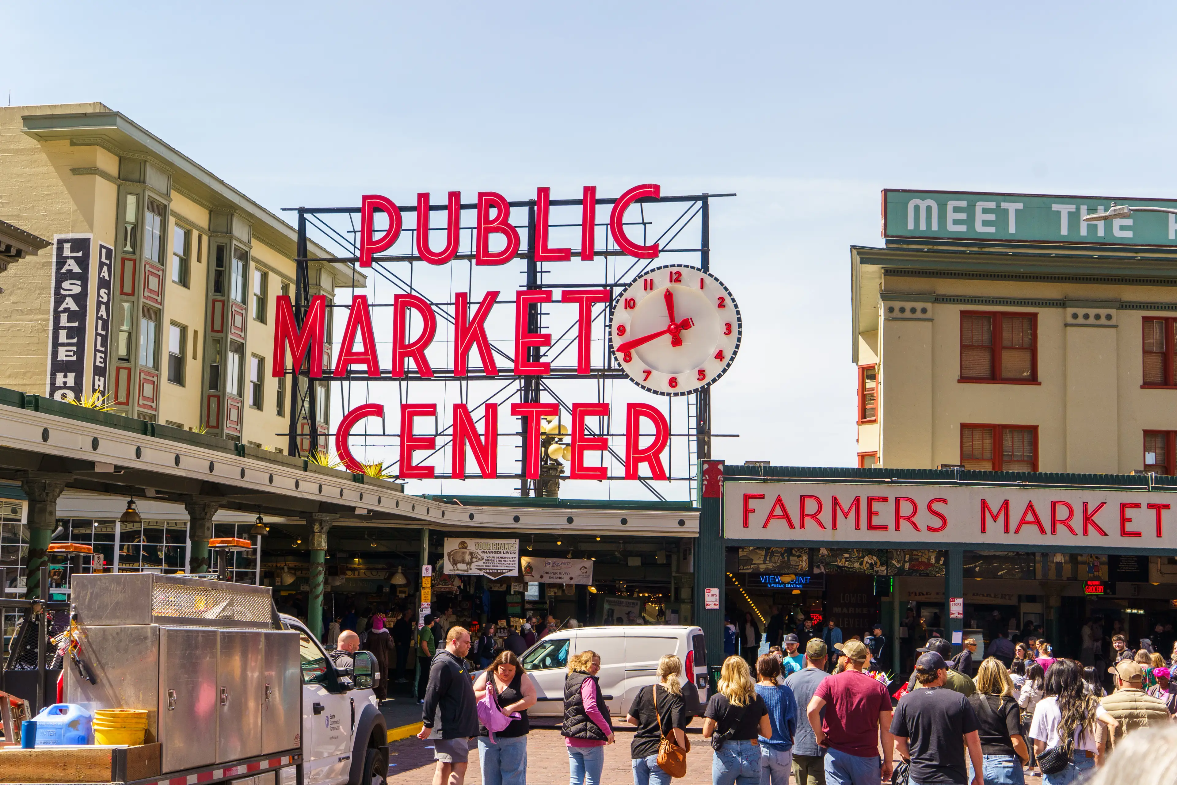 Crowds wander Pike Place Market in Seattle with a bright, red sign above the shops