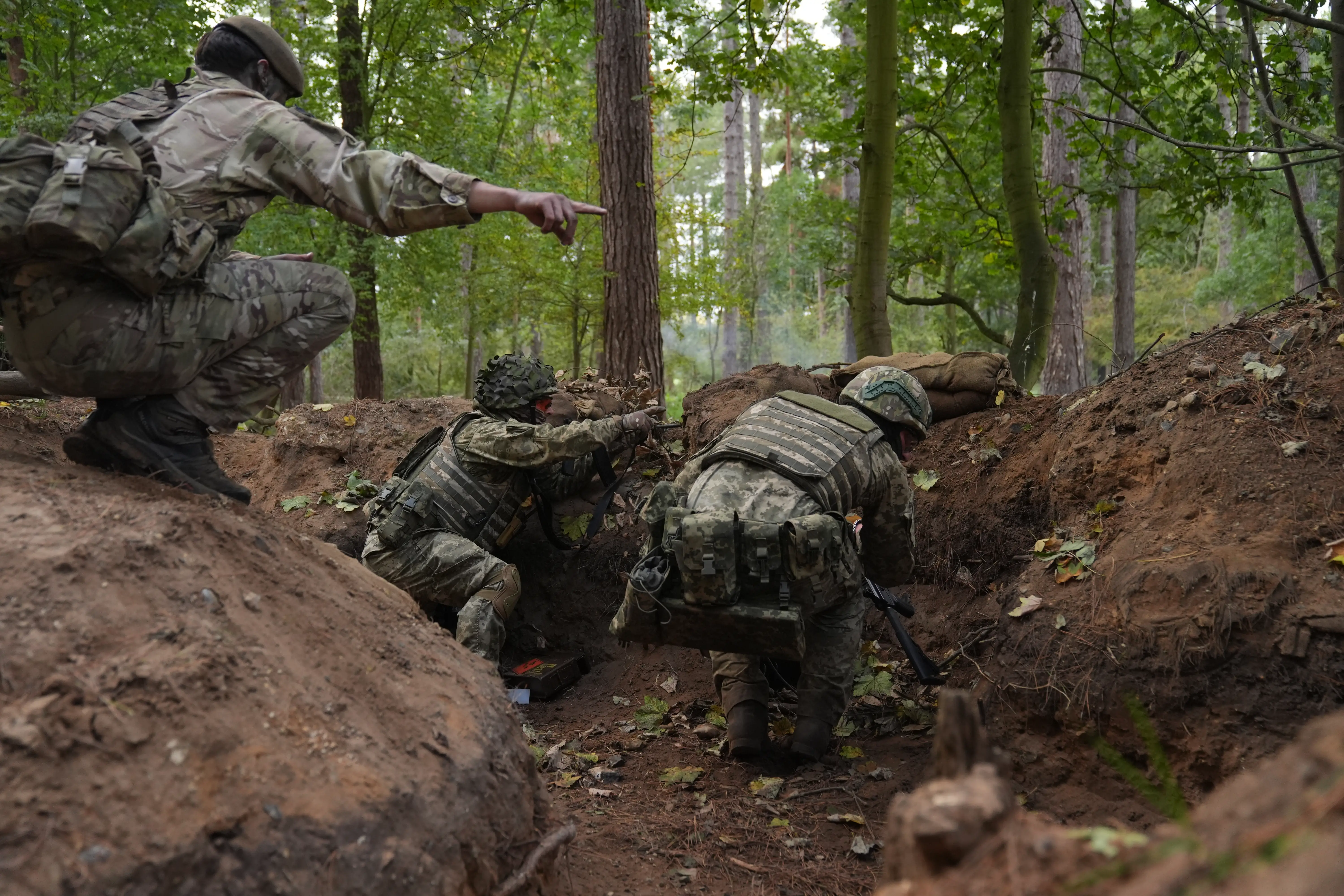 Soldiers crouch and point in a muddy trench