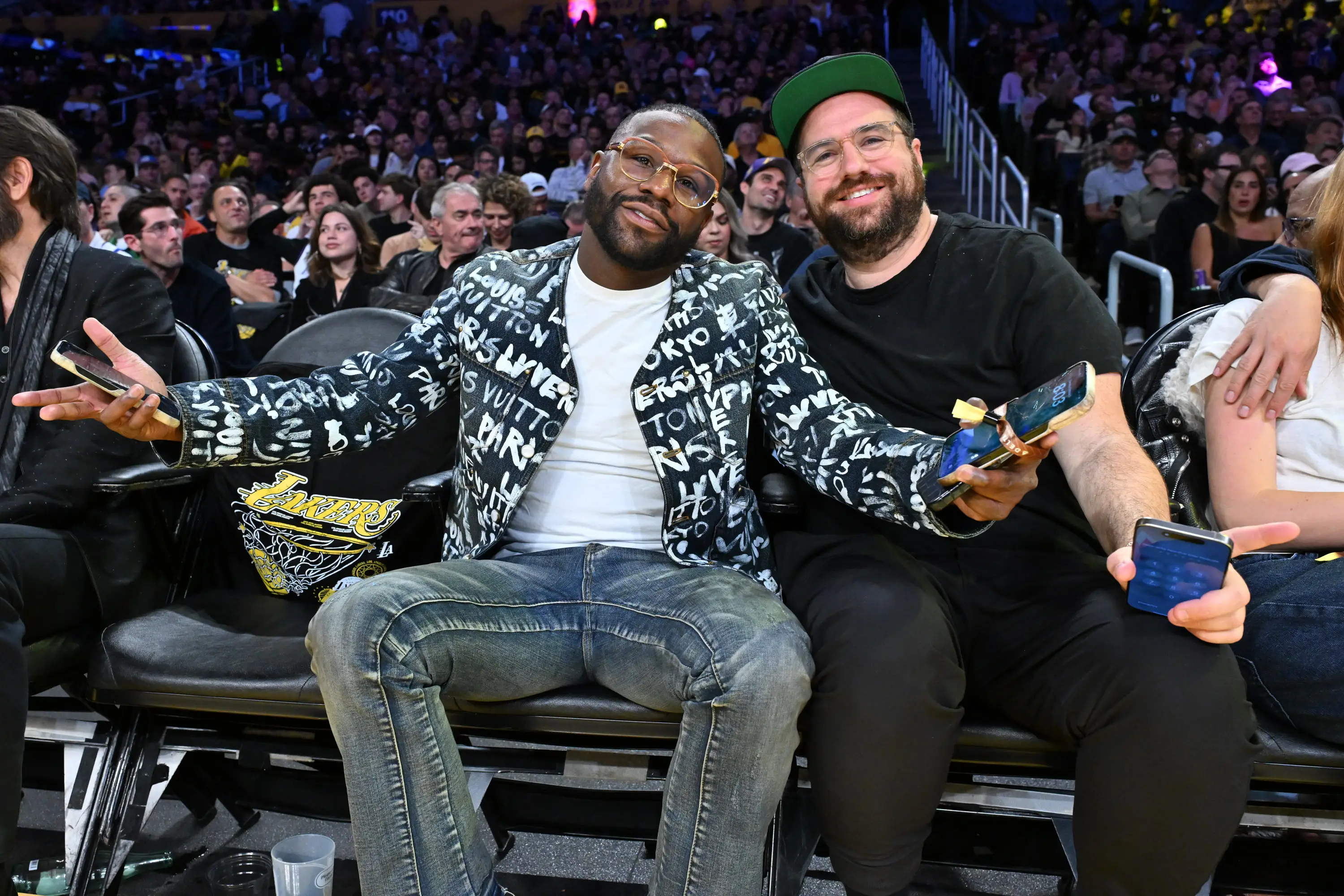 Floyd Mayweather and Jona Rechnitz pose in courtside seats at a basketball game.