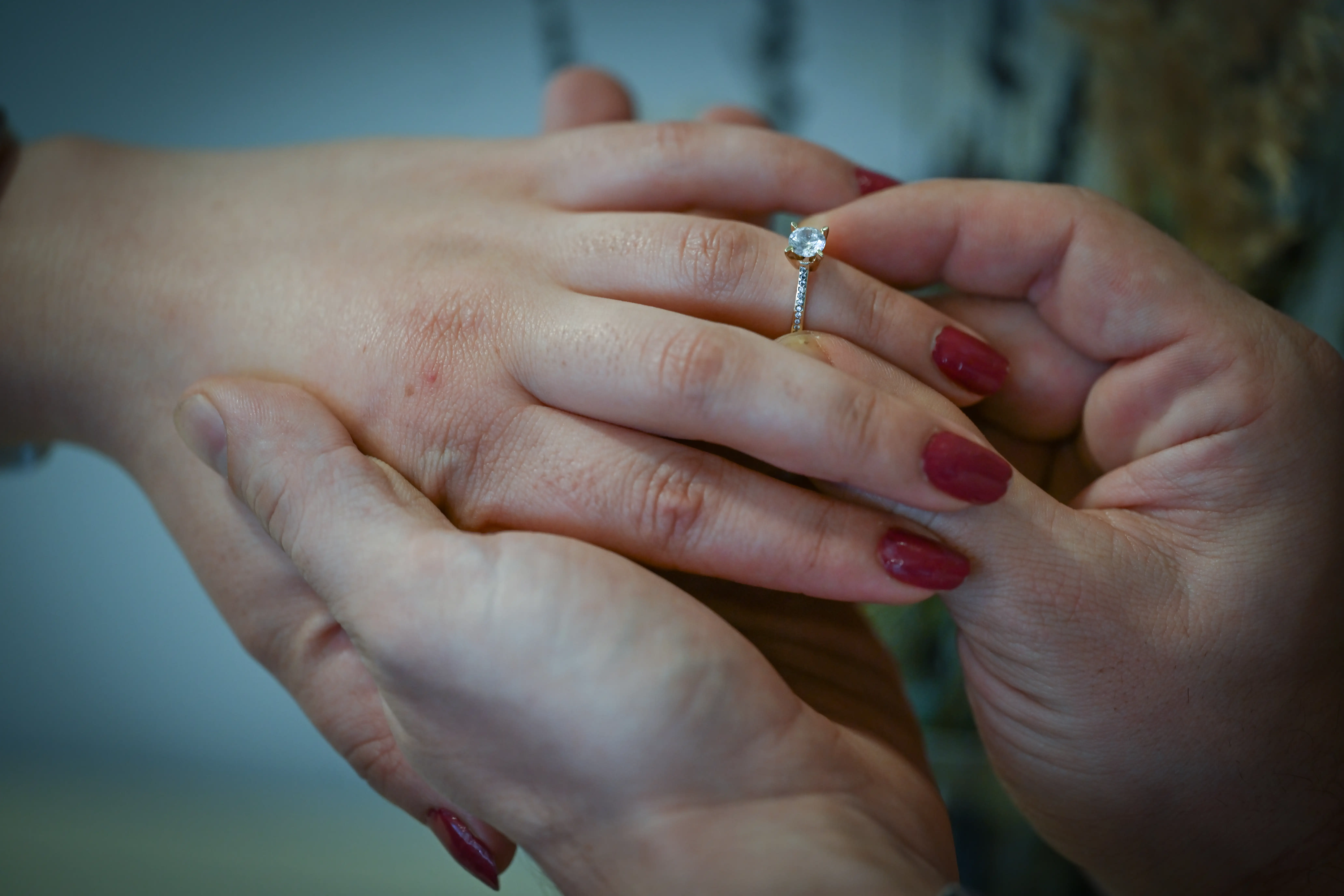 hands putting on a diamond ring on the left hand of another person