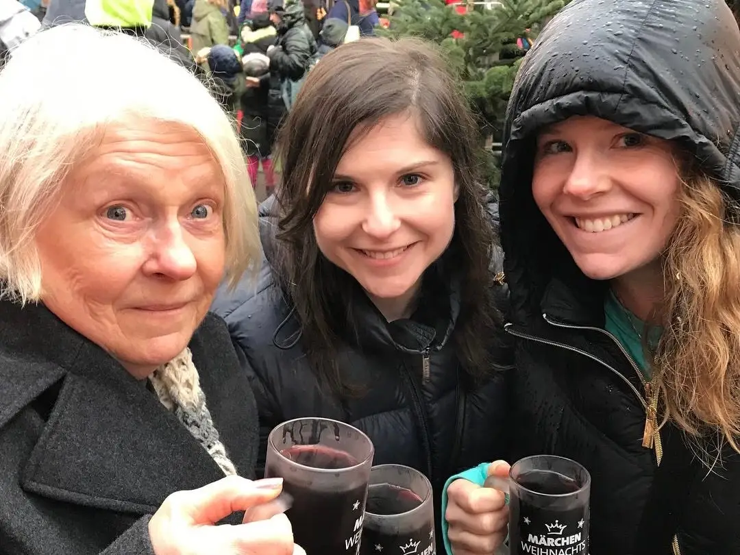 Three women smiling outside holding mugs of dark red liquid