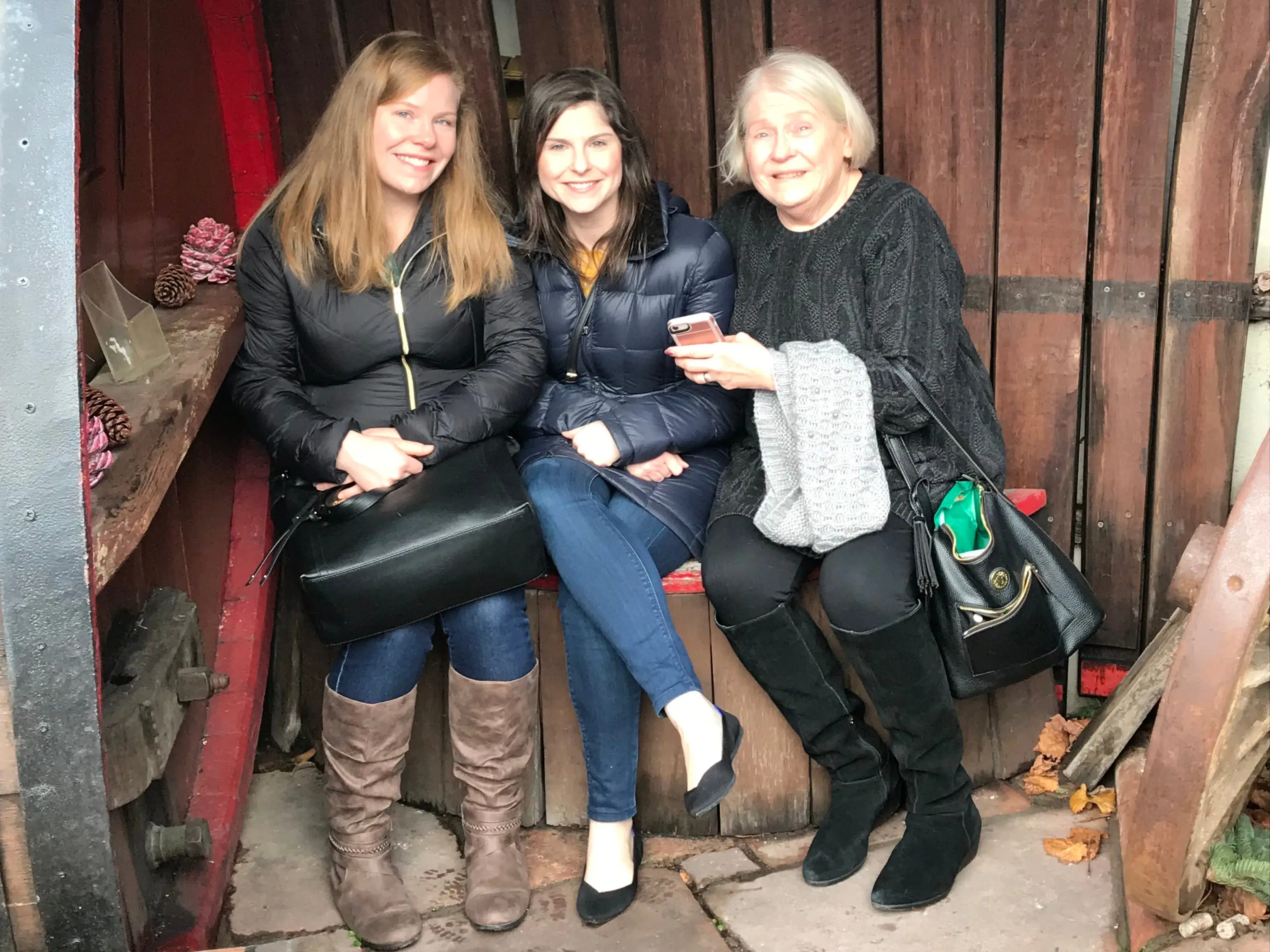 Three women sitting in front of wood panels outside wearing winter jackets