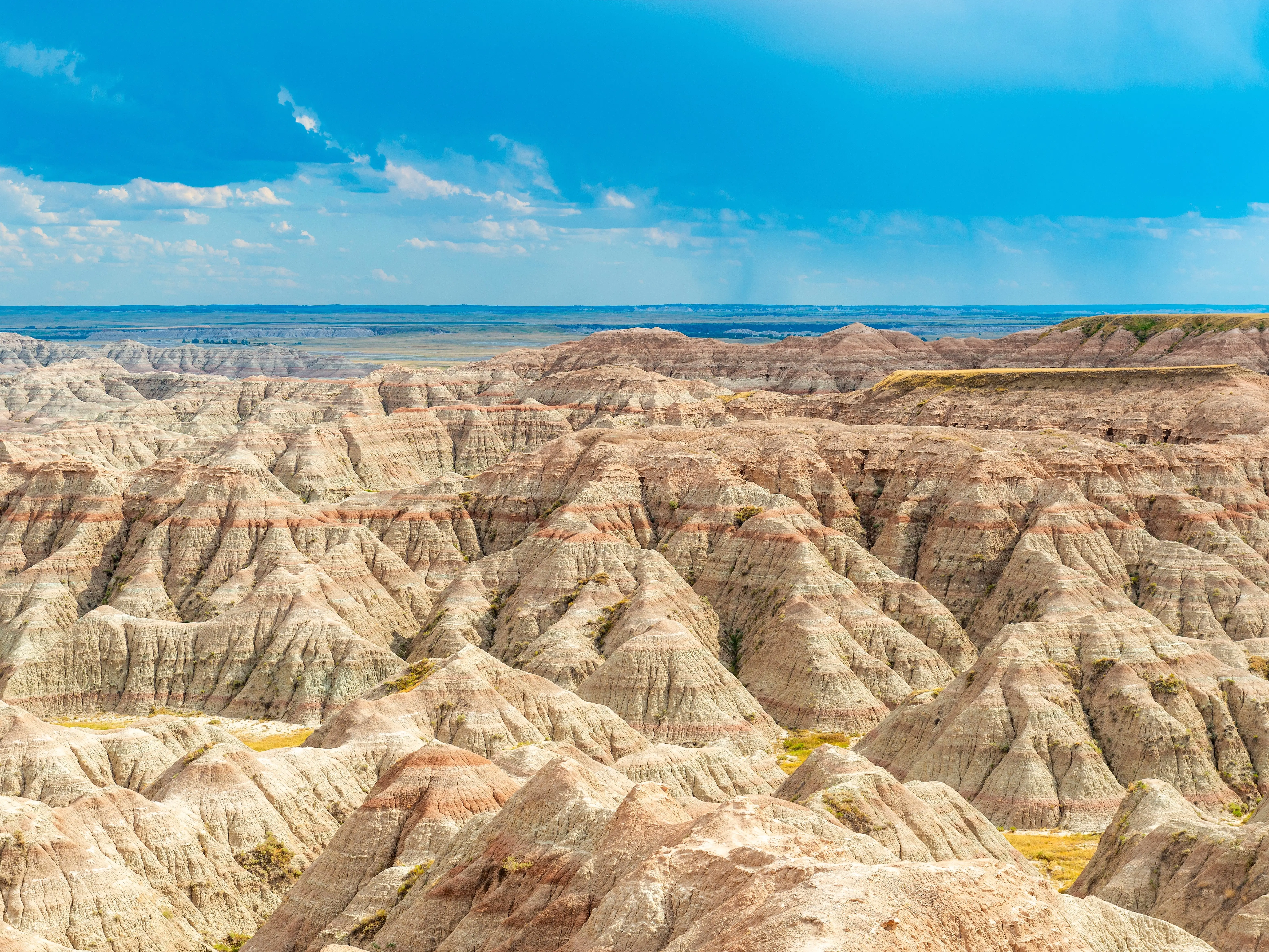 Striped badlands hills under a bright blue sky with scattered clouds.