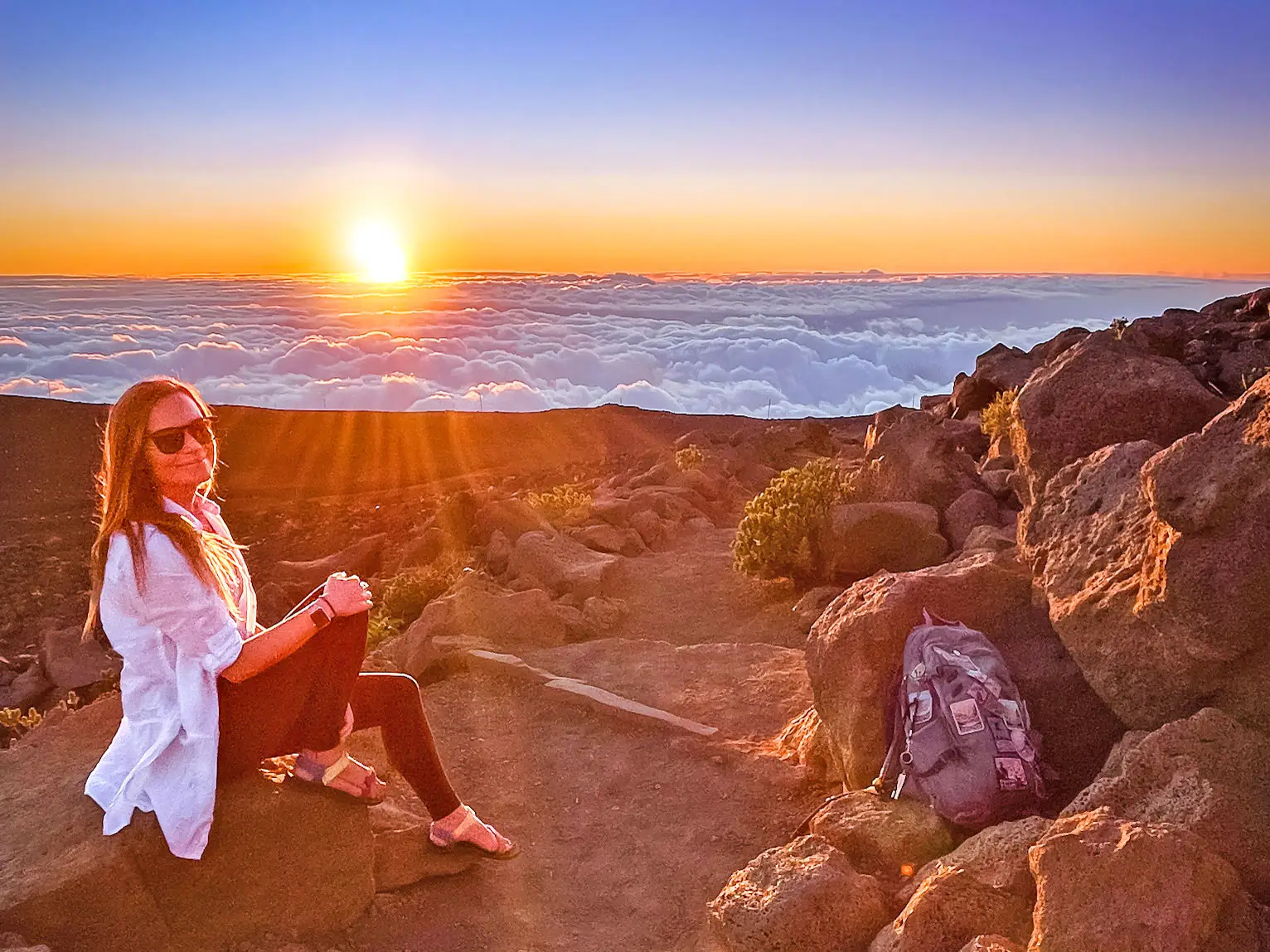 Emily sits on a mountain above the clouds, overlooking the sunset.