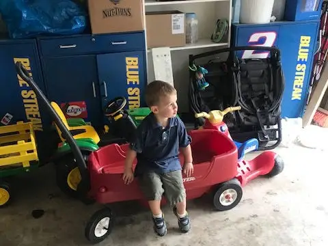 Boy leaning on toy wagon in garage