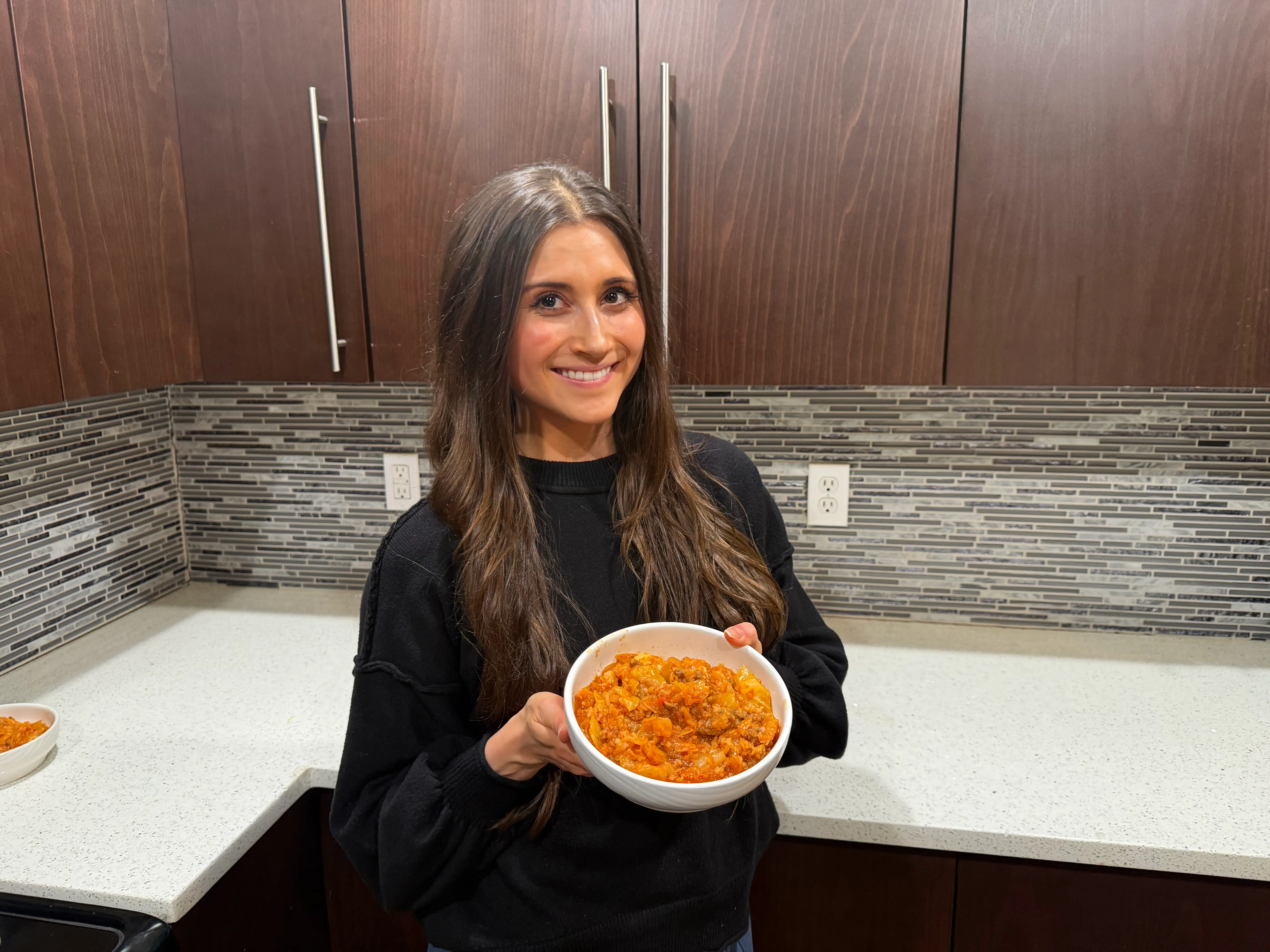 Woman smilingin kitchen holding bowl of cooked cabbage dish