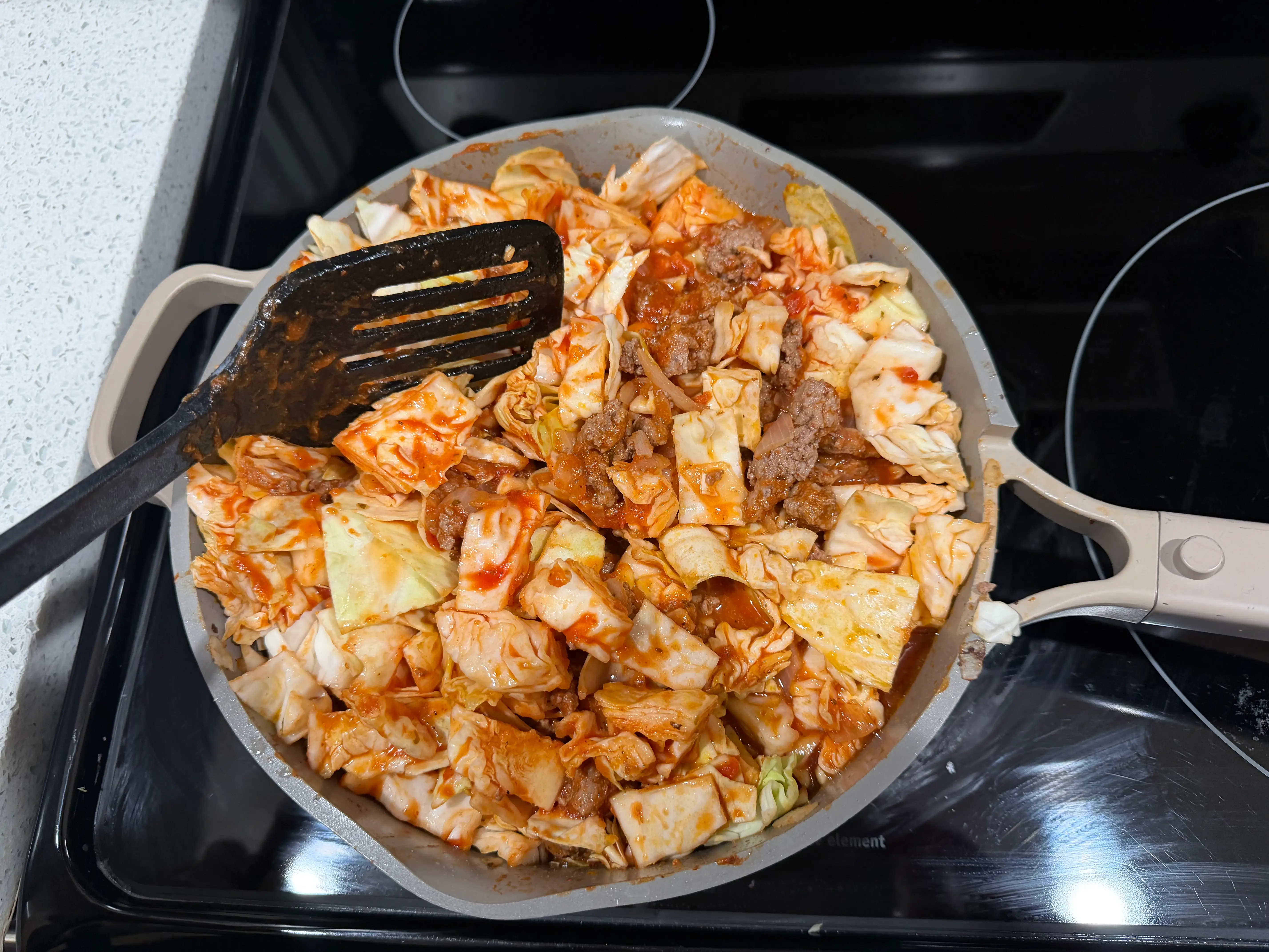 Pan with spatula resting on side with cabbage cooking in sauce