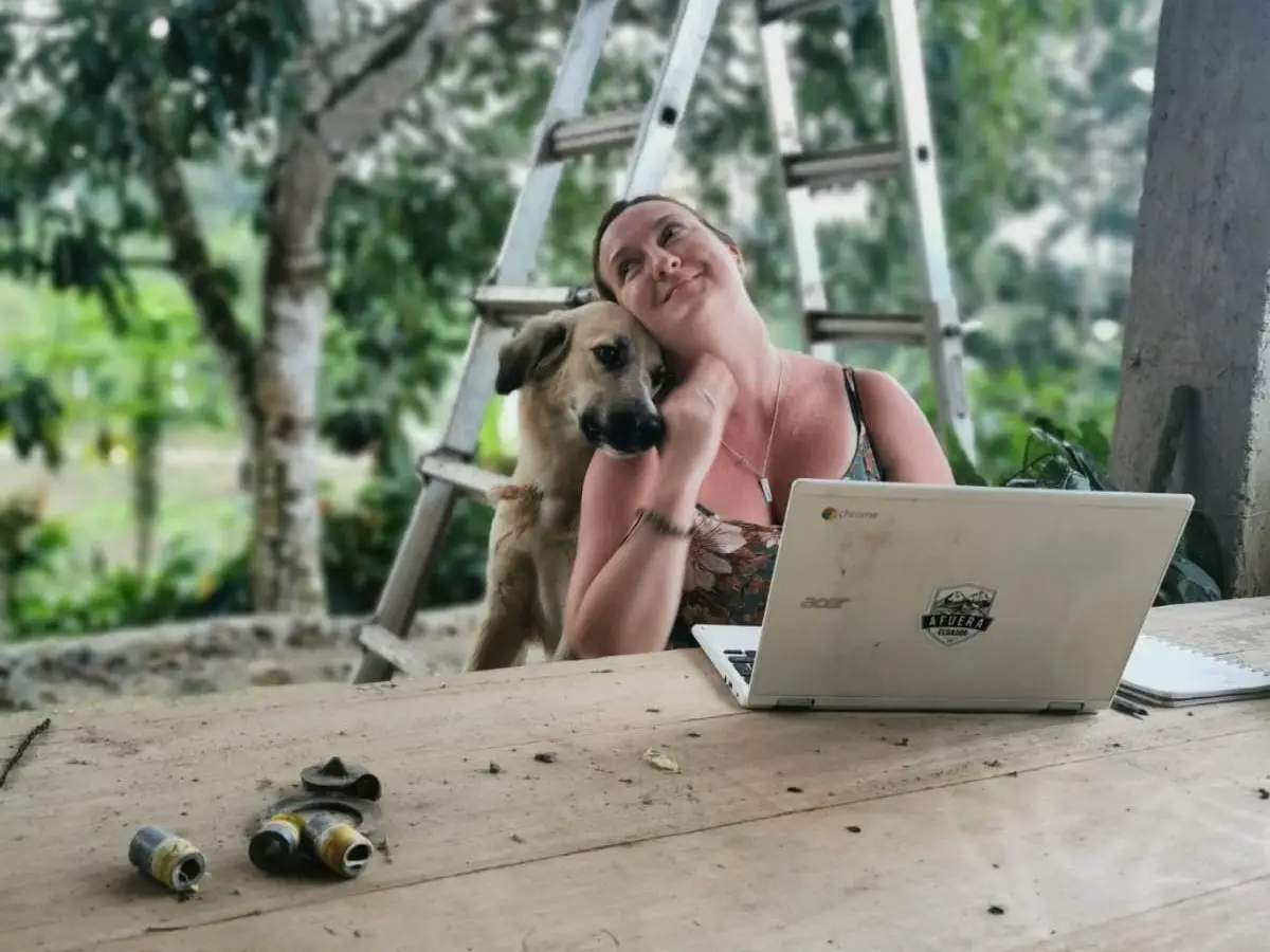 A woman working on a laptop and a dog cuddling up.