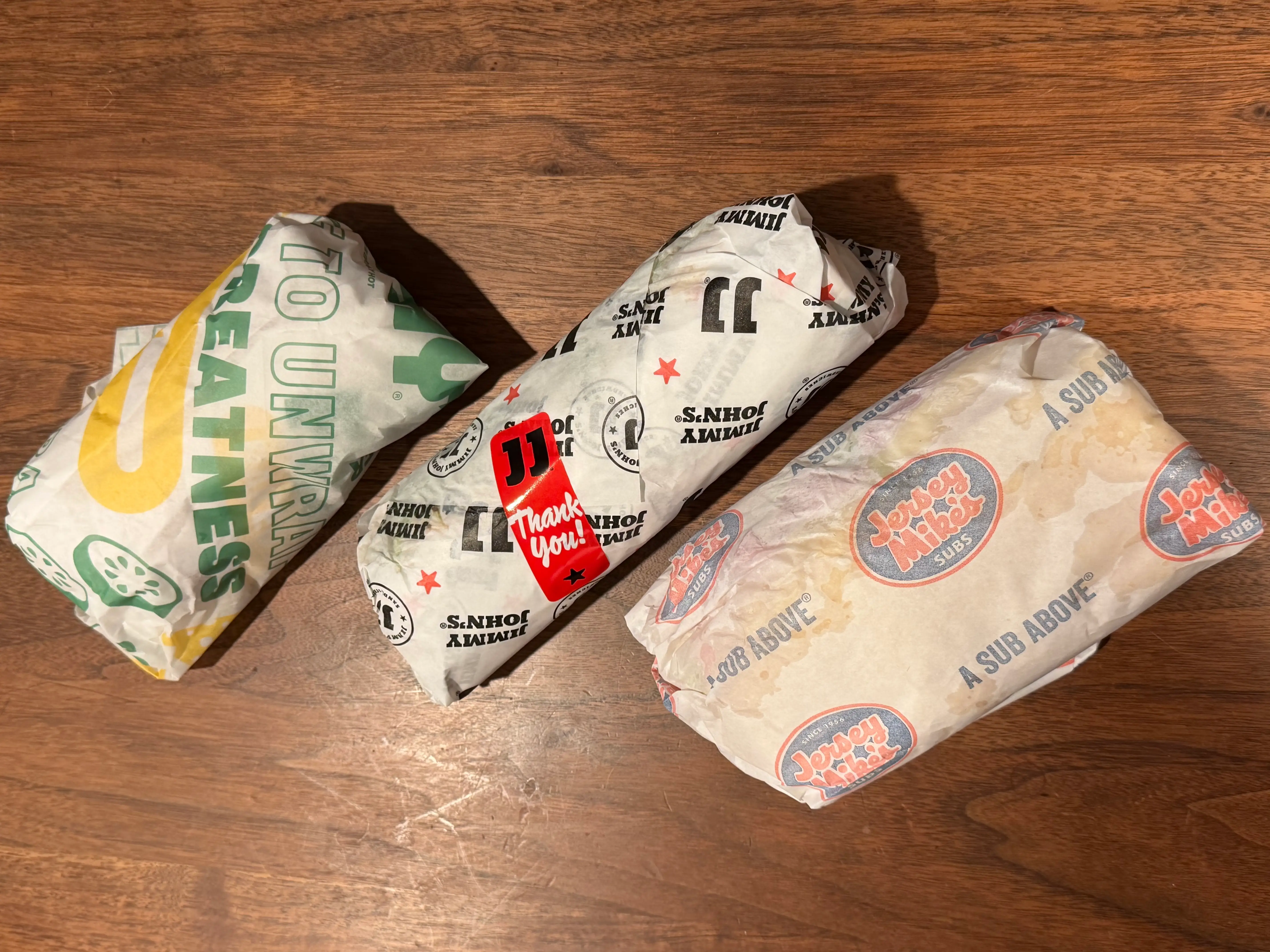Subway, Jimmy Johns, Jersey Mikes sandwiches in wrappers on table