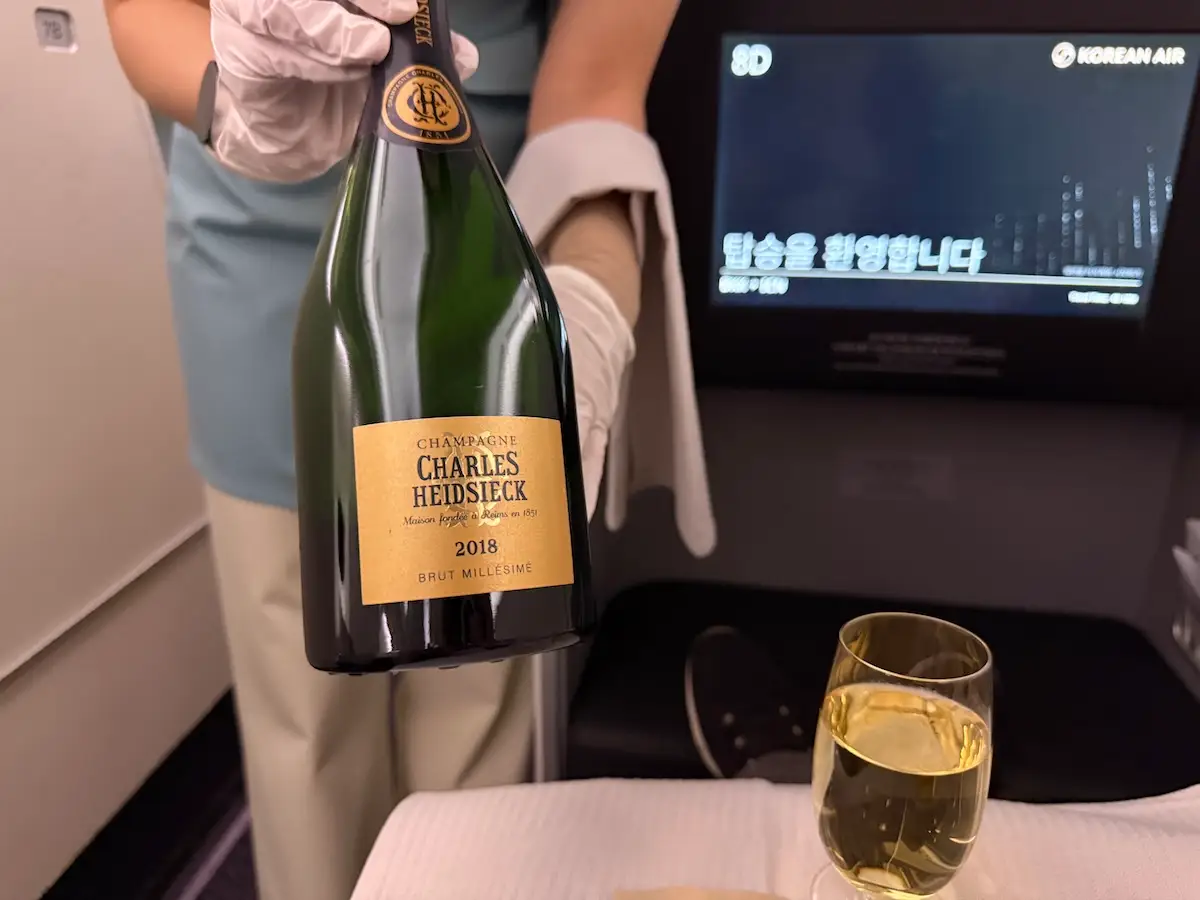 Hand holding Charles Heidsieck 2018 brut millesime champagne. next to glass of it on plane