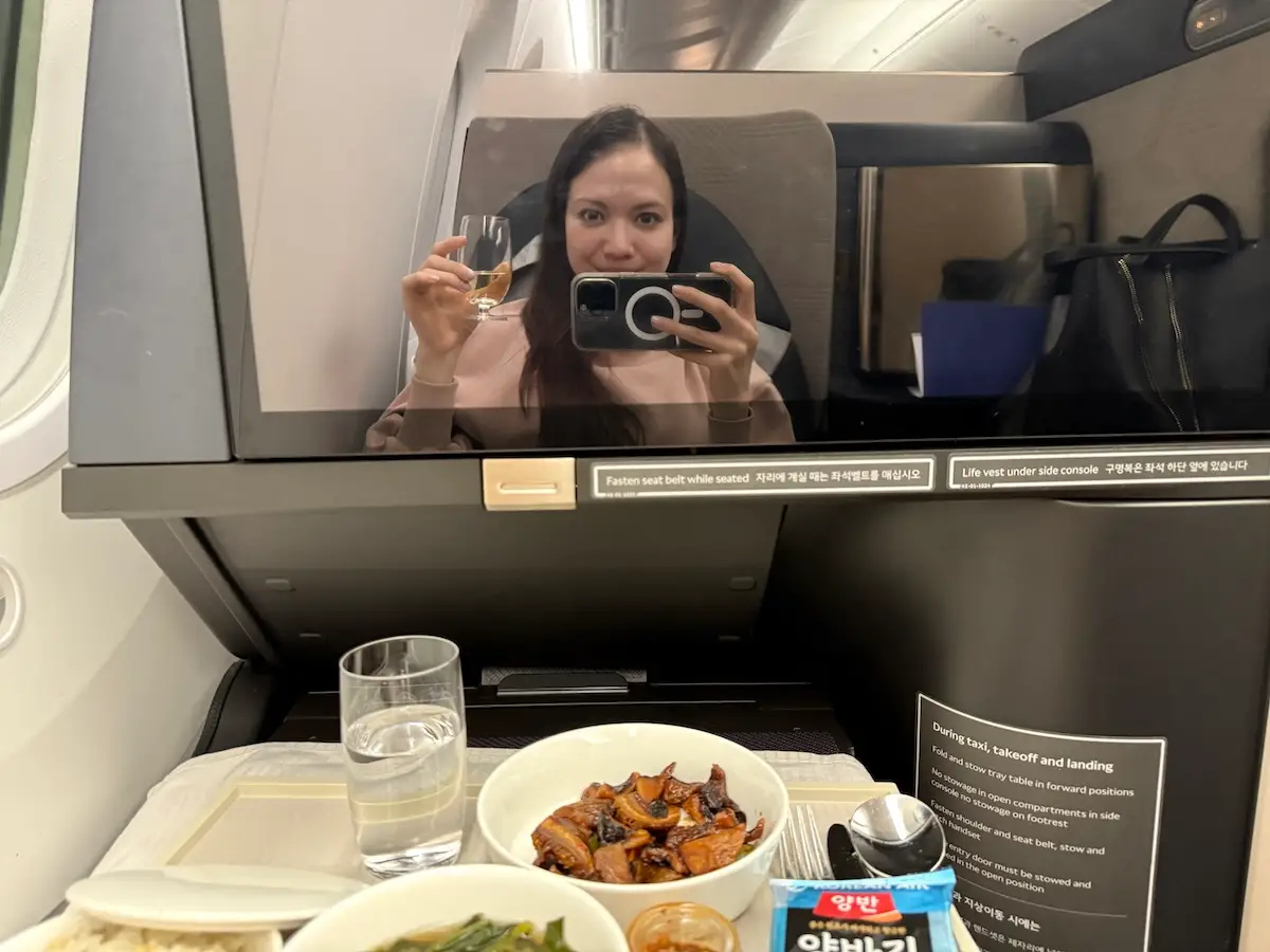 Woman smiling taking selfie in mirror with tray table full of food below