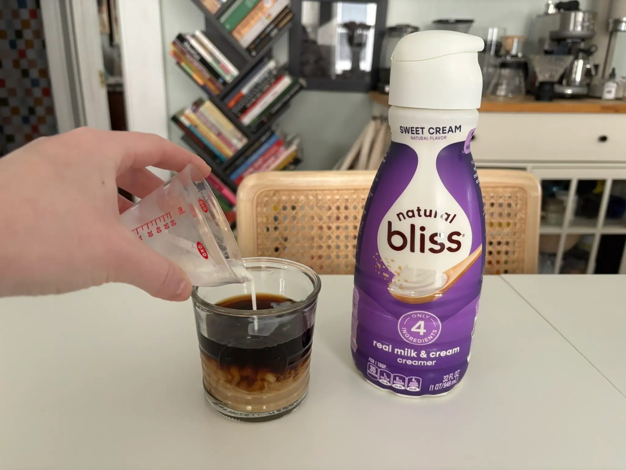 Natural Bliss sweet cream creamer next to cup of coffee with cream being poured into it
