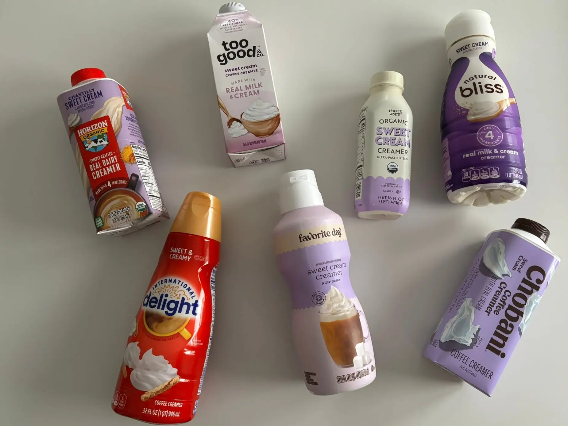 Sweet cream coffee creamers from Horizon, International Delight, Too Good & Co, Favorite Day, Trader Joe's, Natural Bliss, and Chobani laid out on table