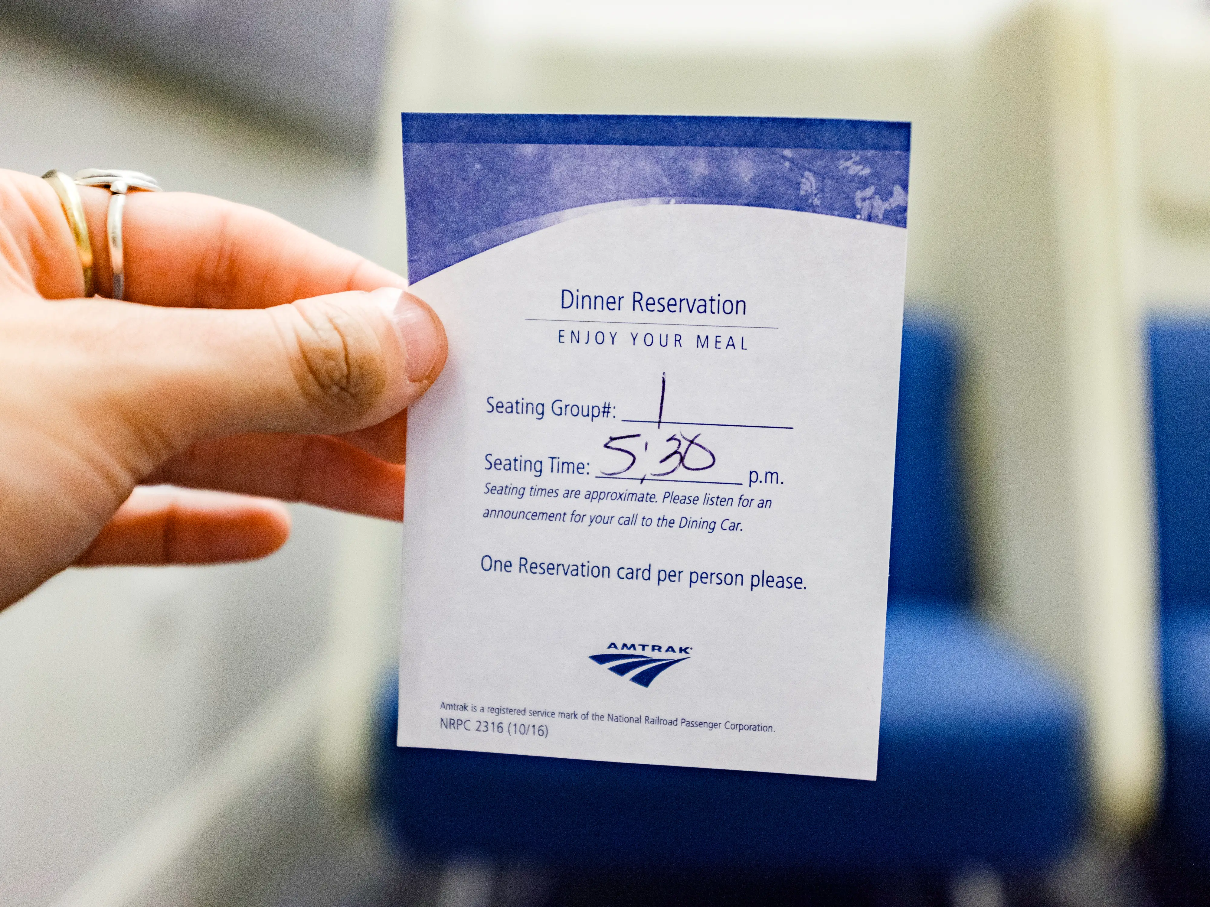 A hand holds a slip of paper with a 5:30 p.m. dinner reservation on it