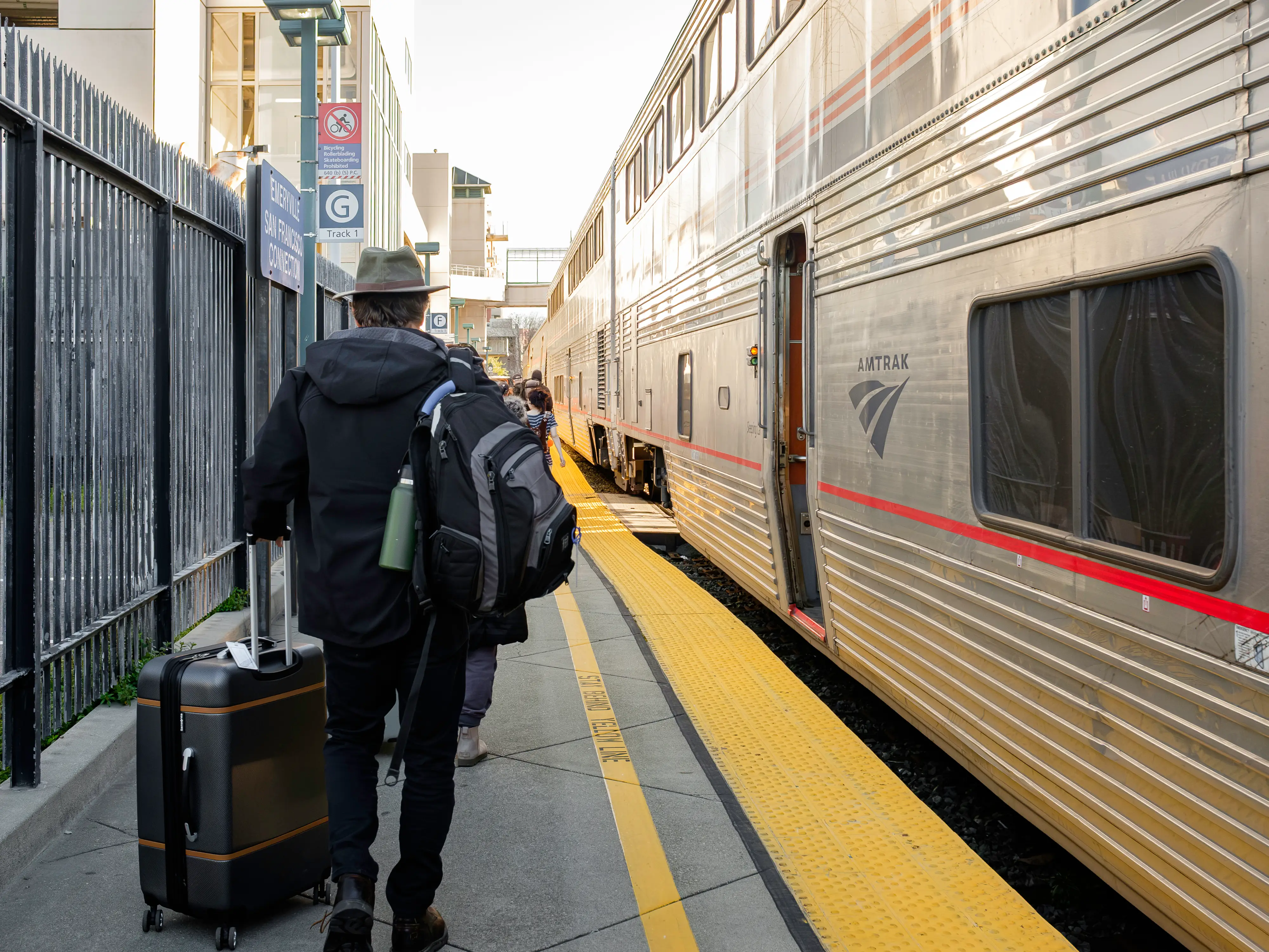 An outdoor train platform with a line of travelers walking on the left and a train on the right
