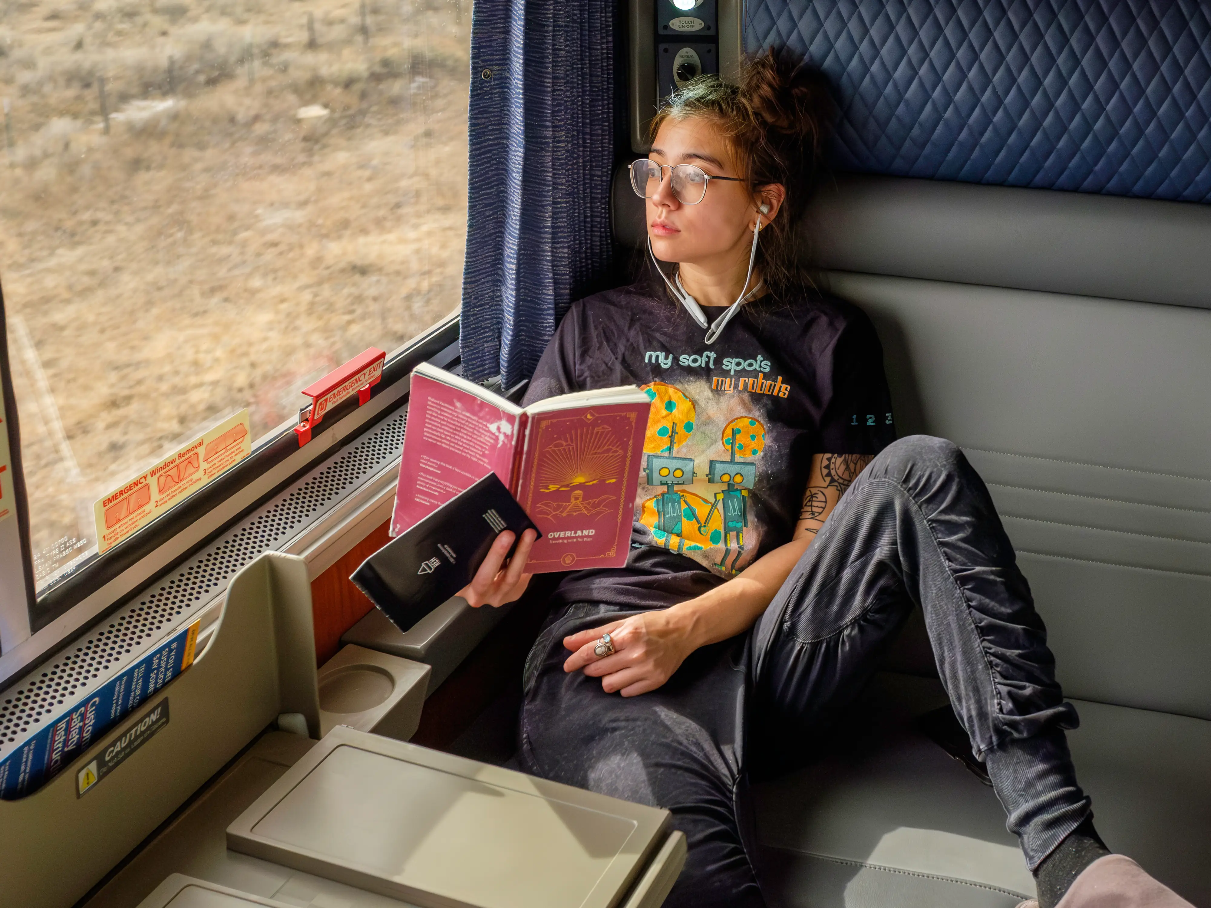 The author sits in an Amtrak bedroom holding a red book while looking out a window on the left