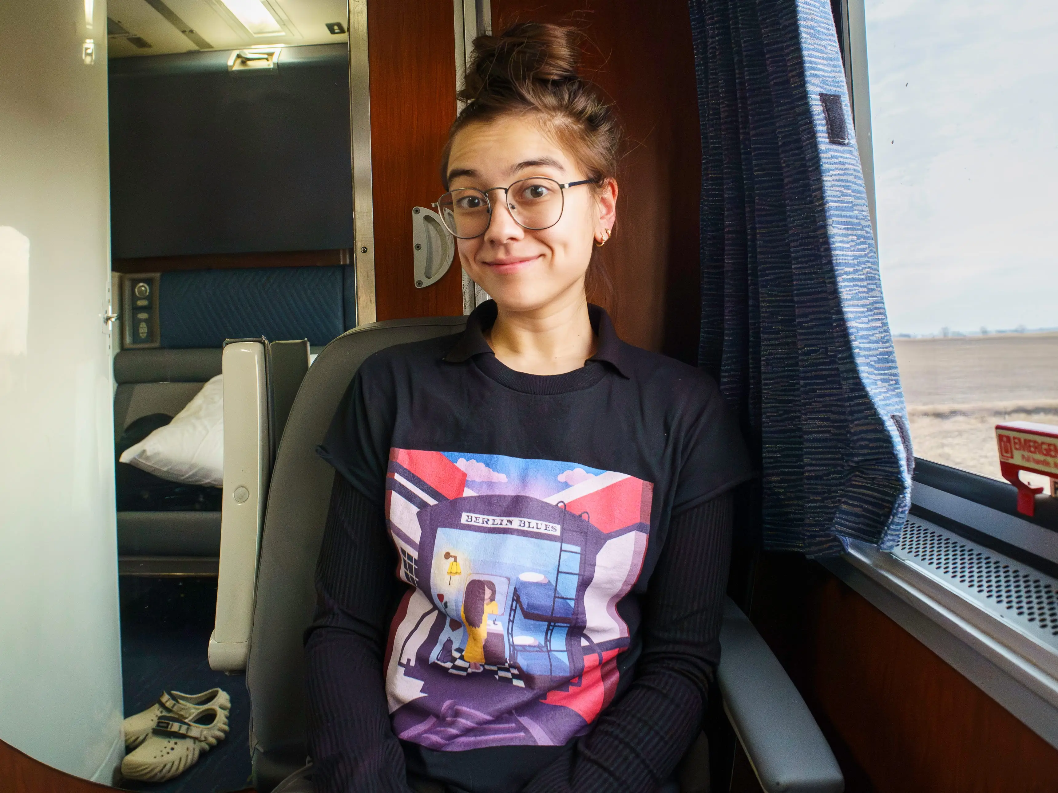 The author sits in an Amtrak bedroom with a mirror on the left back wall and a window on the right