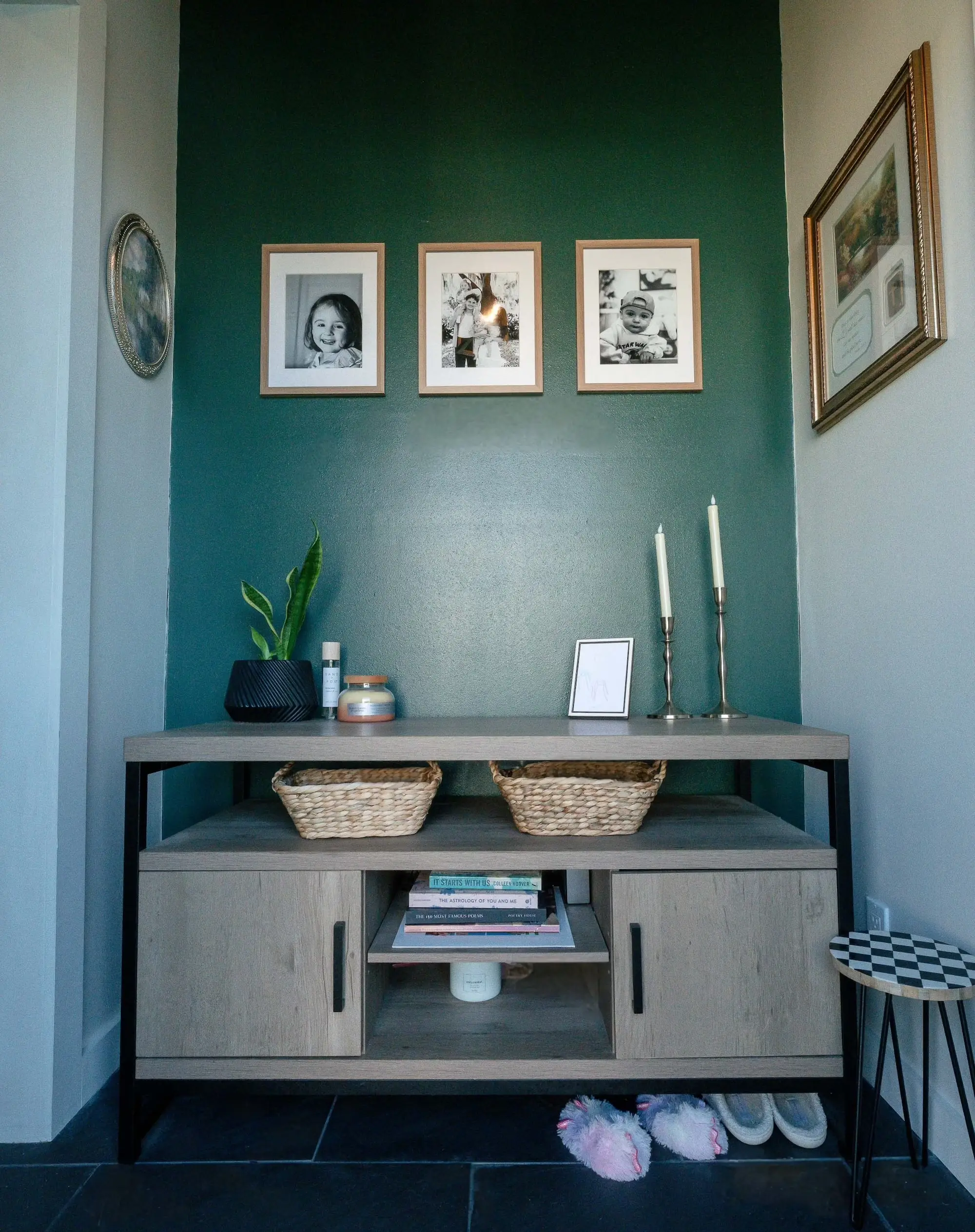 An entryway to a home with a green wall, pictures on the walls, and a shelving unit.