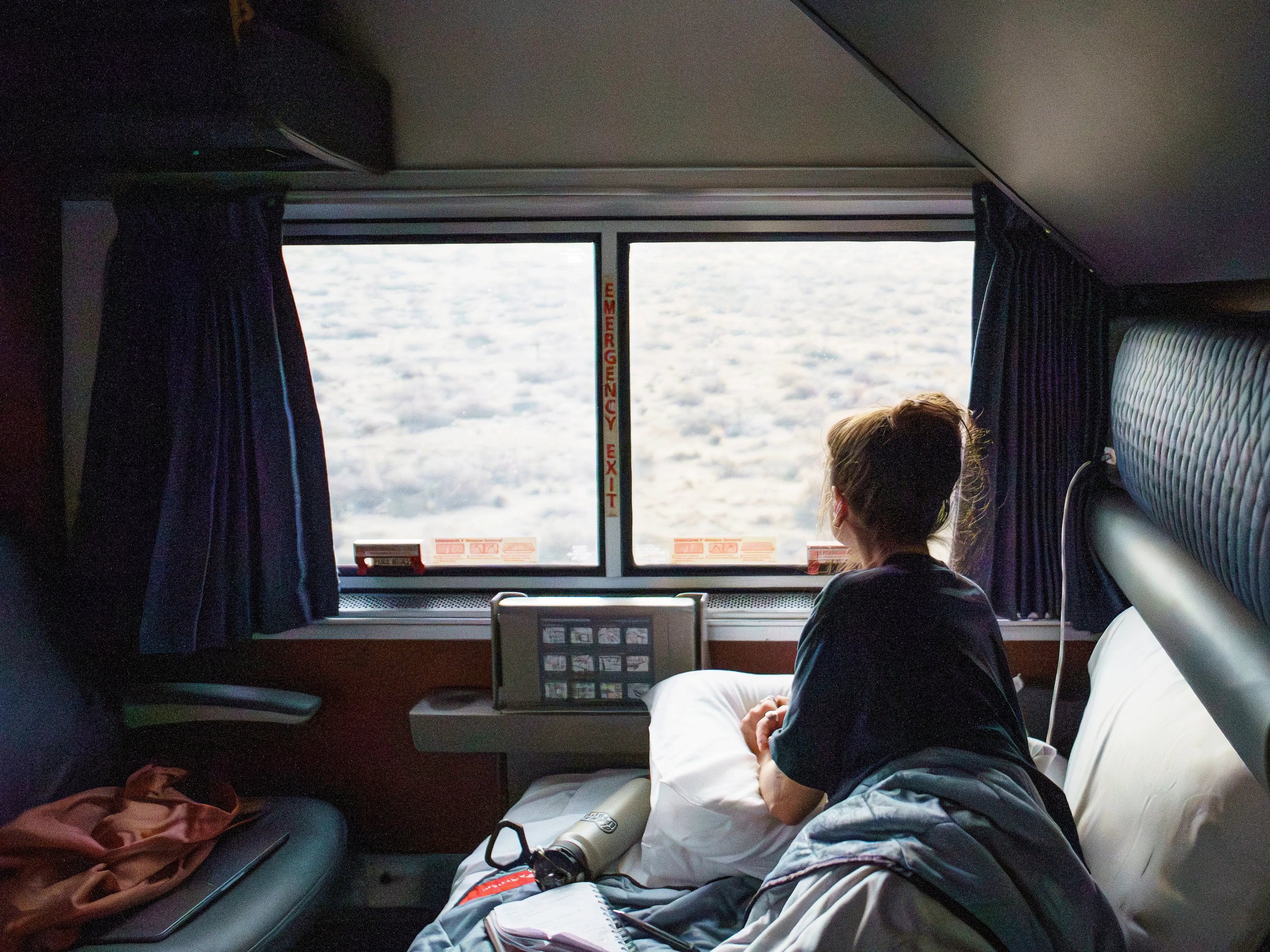 The author lays in a lower bunk looking out the window in an Amtrak train bedroom