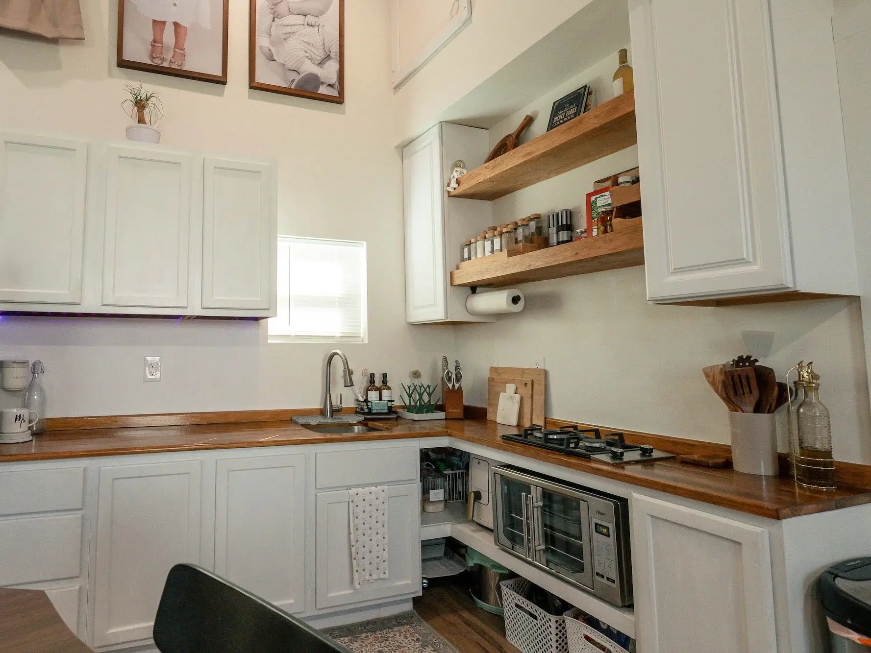 A kitchen with white cabinets, butcher block countertops, and wood open shelving.