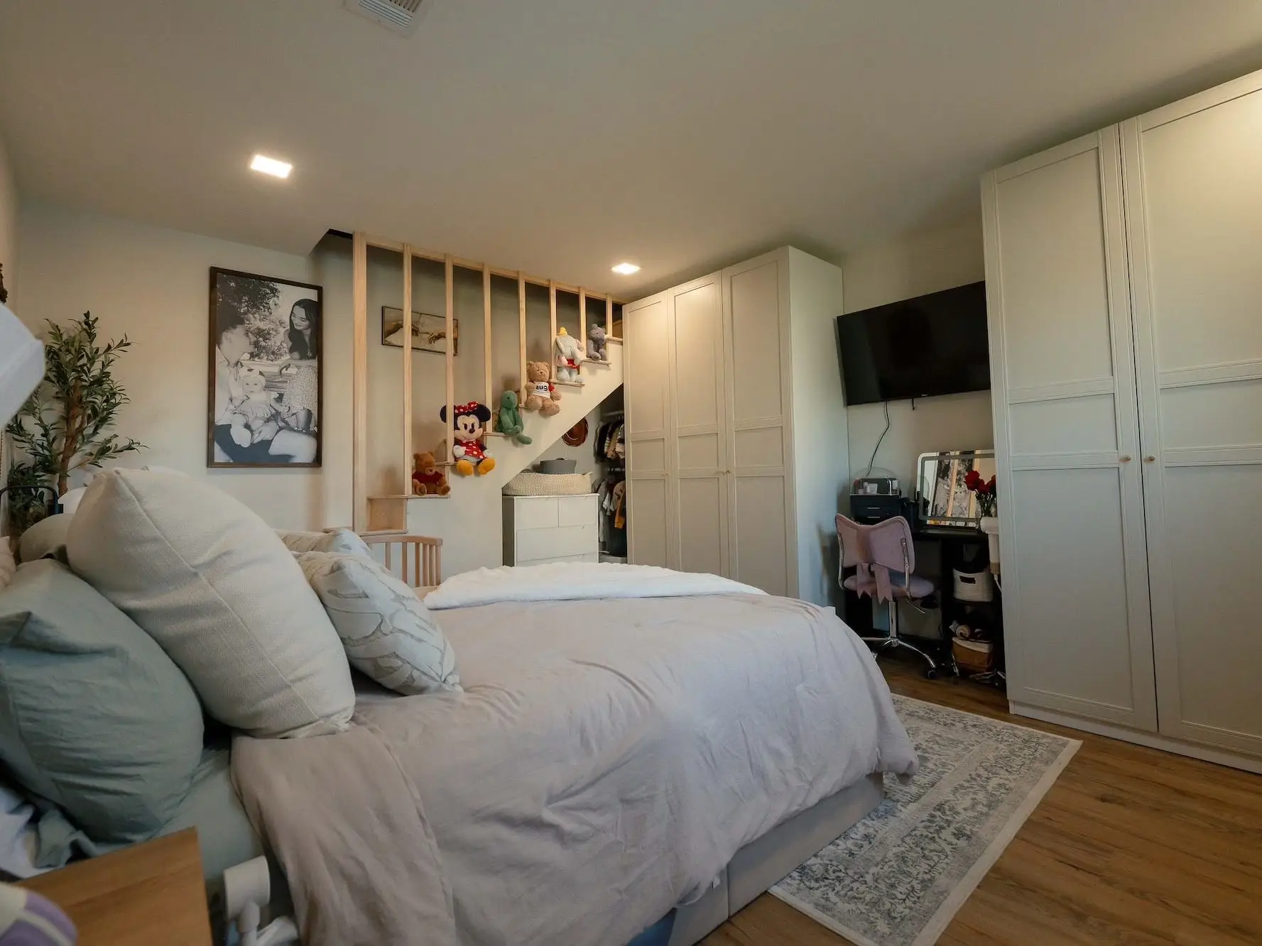 A bedroom with built-in cabinetry, a queen-sized bed, and a staircase leading to a loft.
