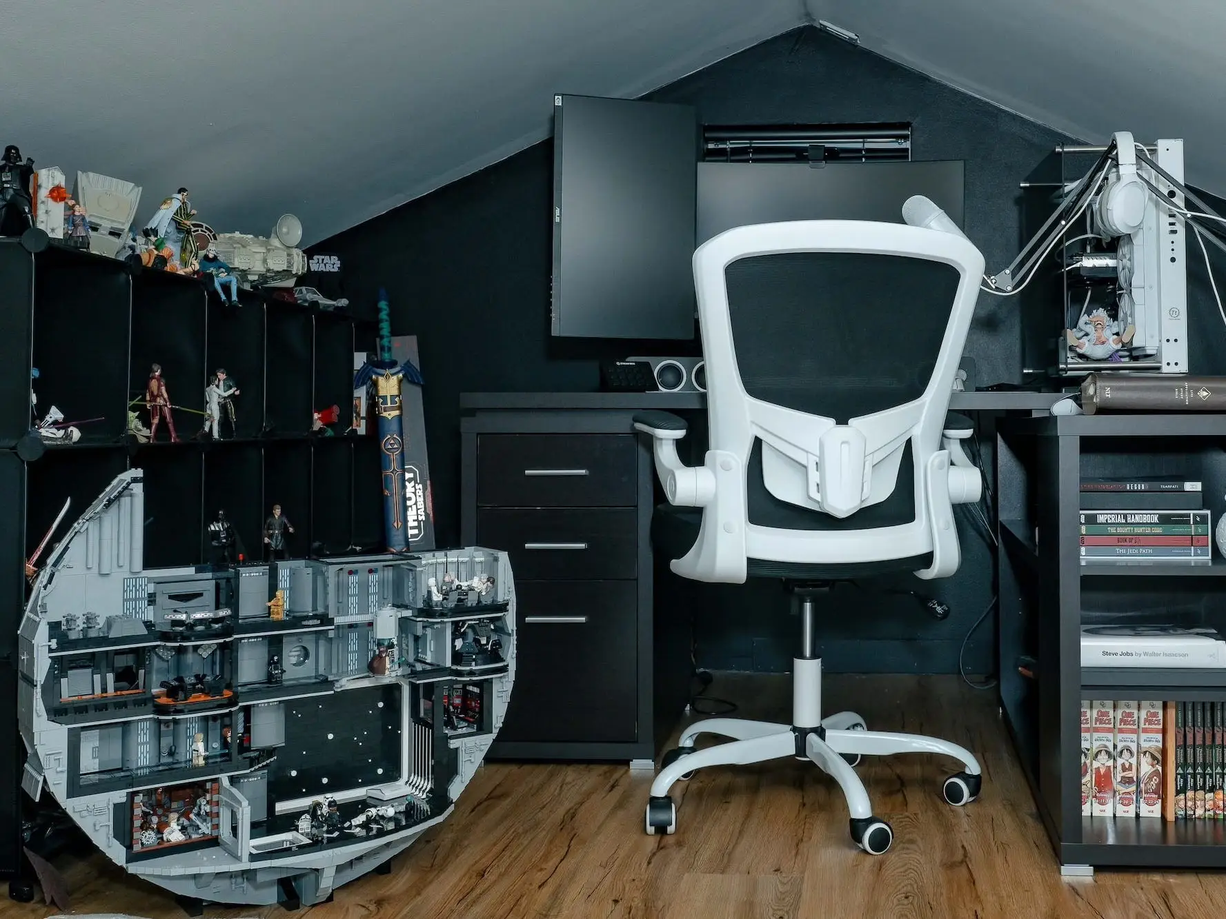 A loft study with a black desk, a computer setup, and collectibles.