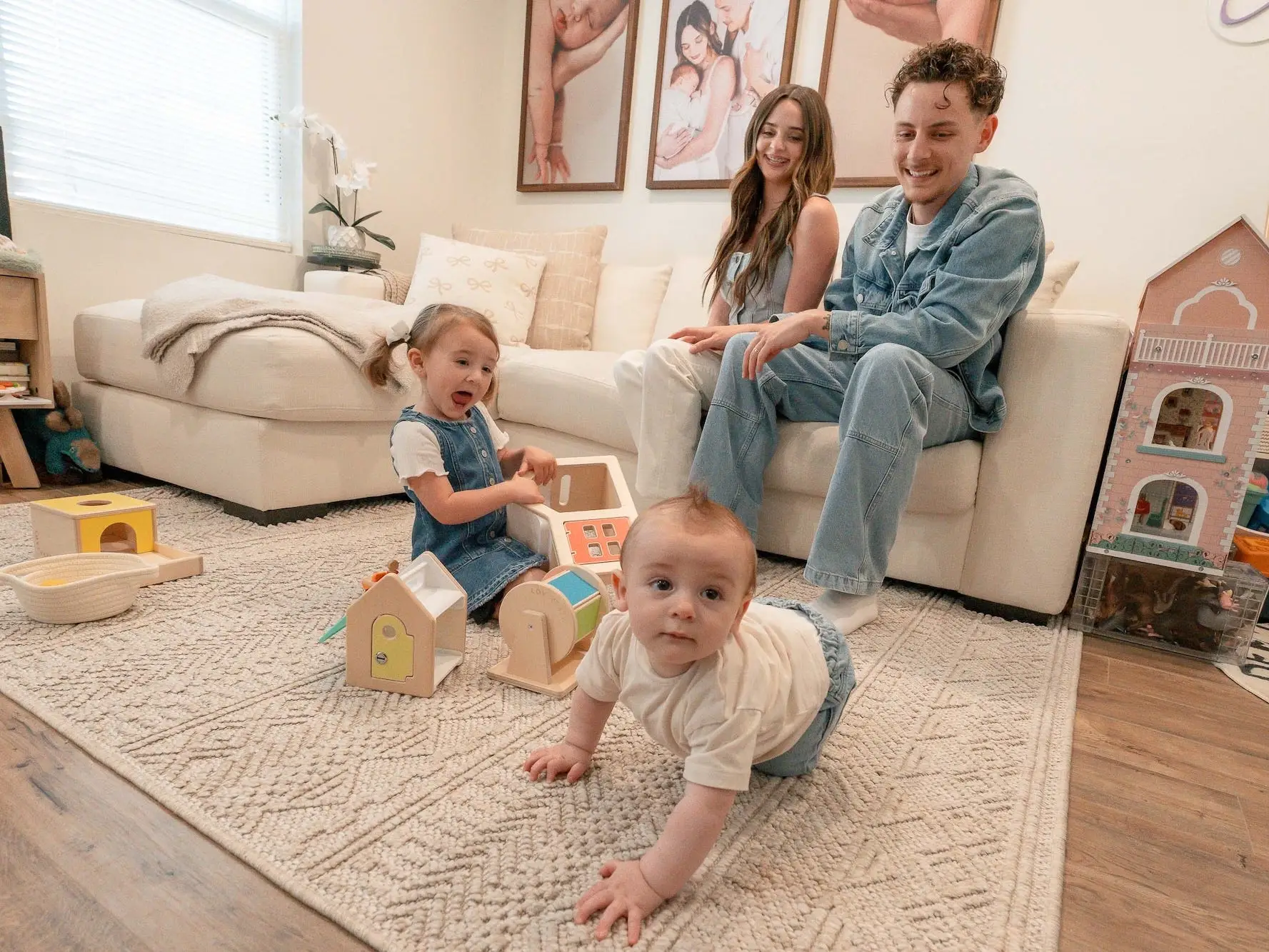 A couple sits on a couch and watches their two children play on the floor in front of them.