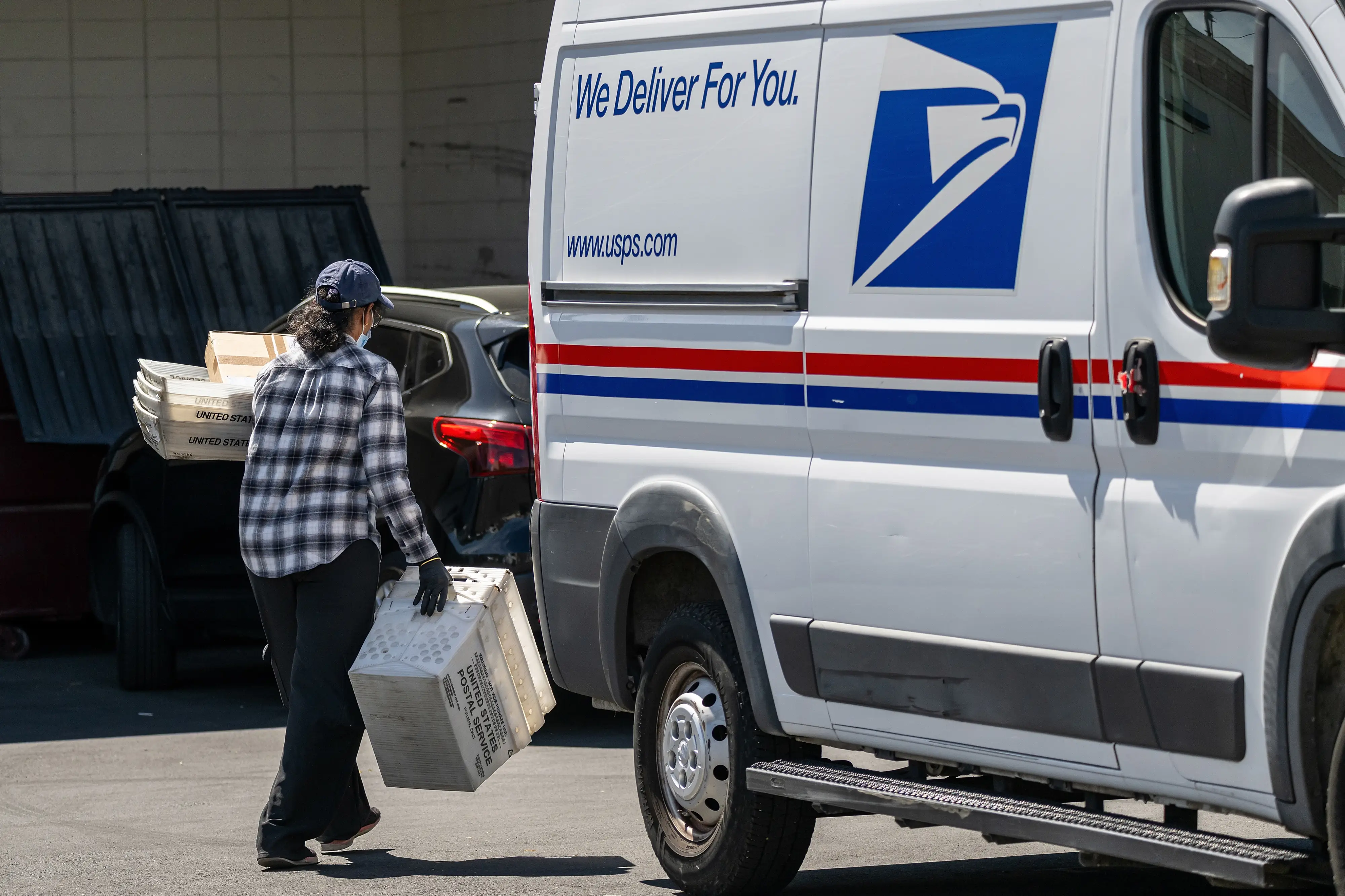 A United States Postal Service (USPS) worker carries containers and packages from a vehicle in Tracy, California, US, on Wednesday, March 25, 2026.