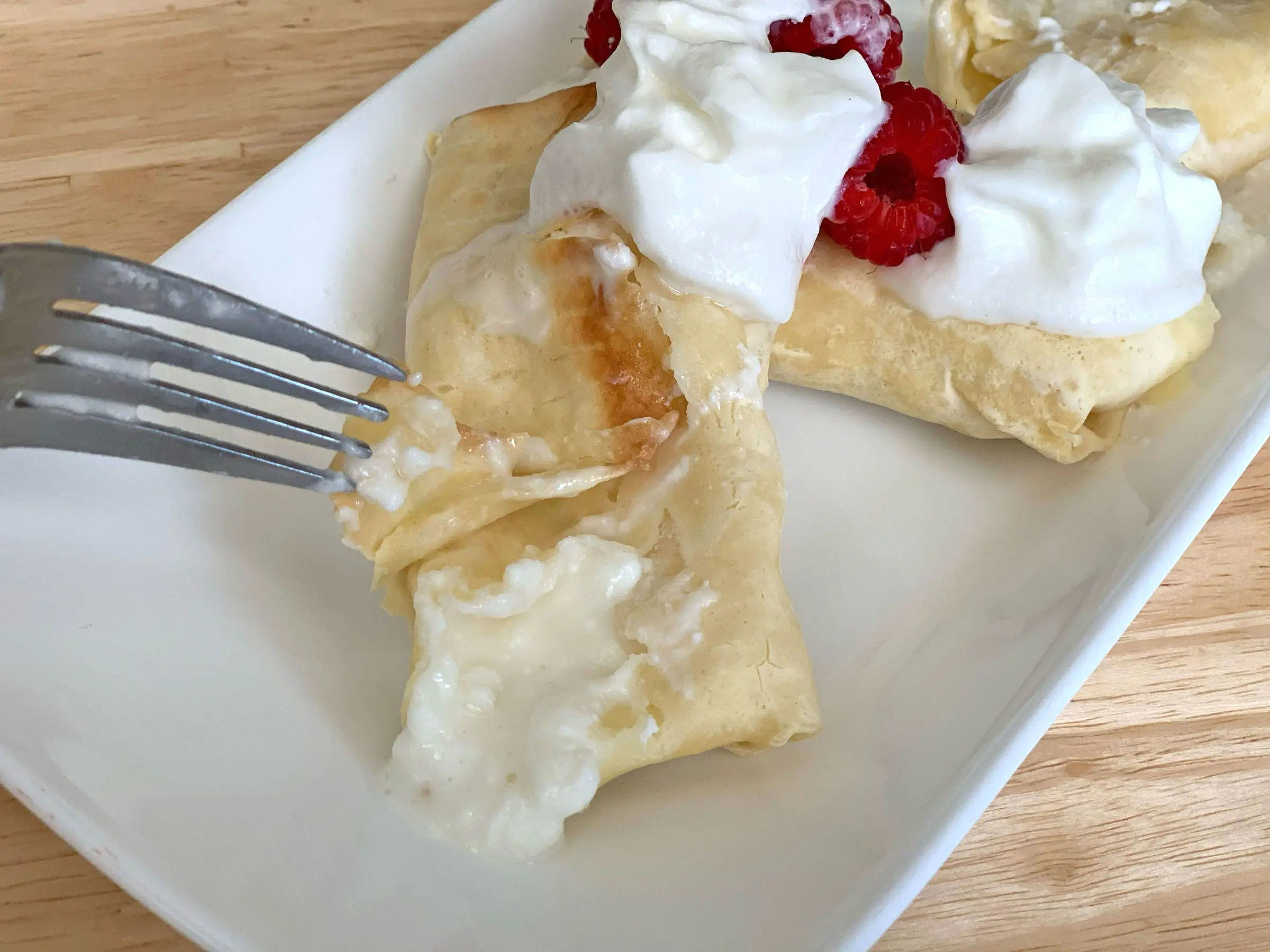 A fork cutting open Trader Joe's blintzes on a white plate.